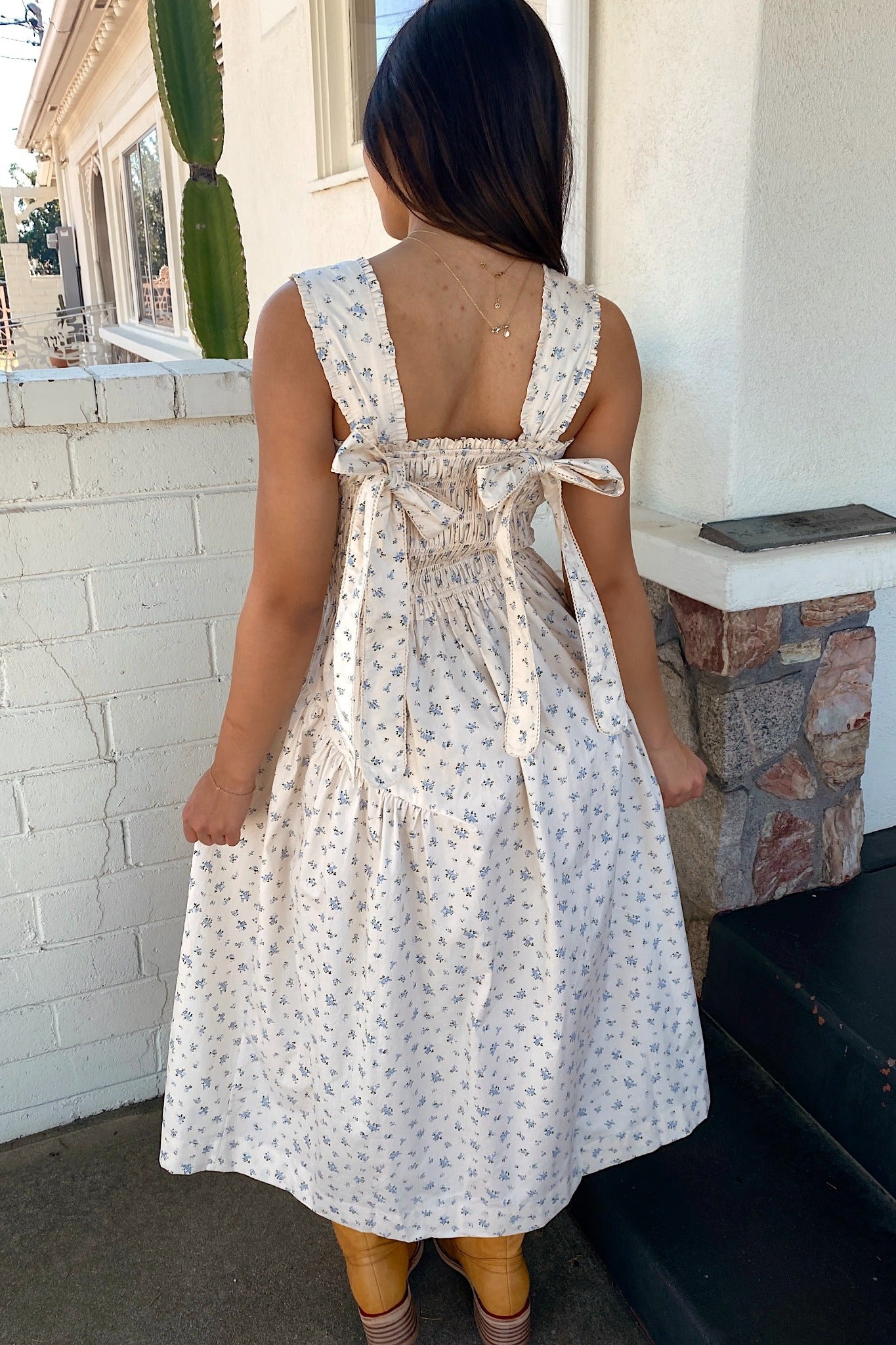 Woman wearing a white floral dress standing on a porch.