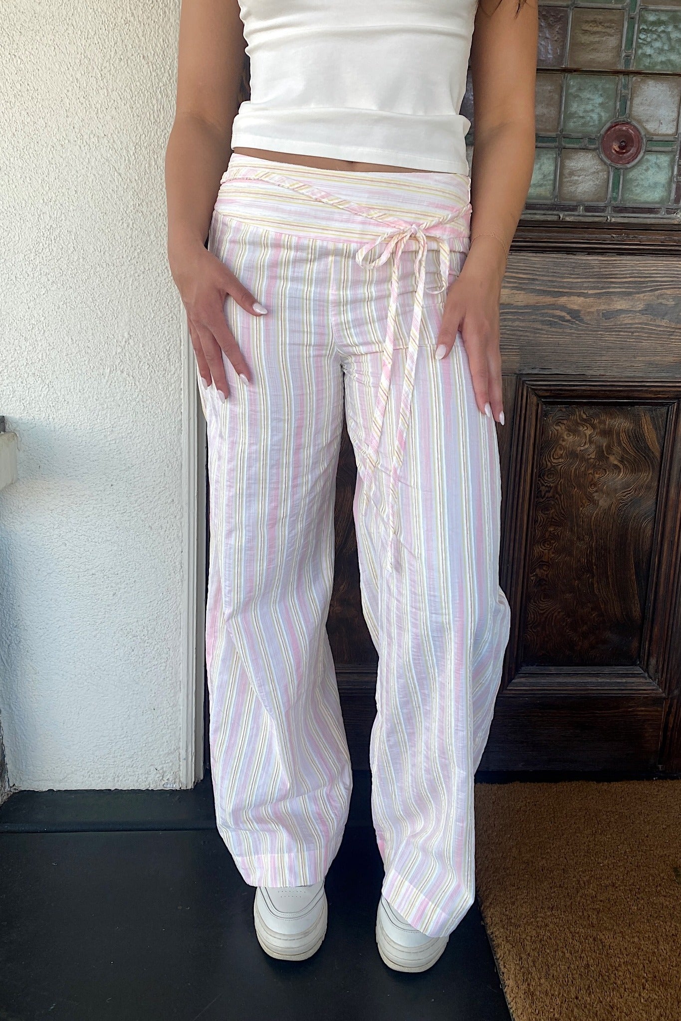 Person wearing white striped pants and a white top in front of a wooden door.
