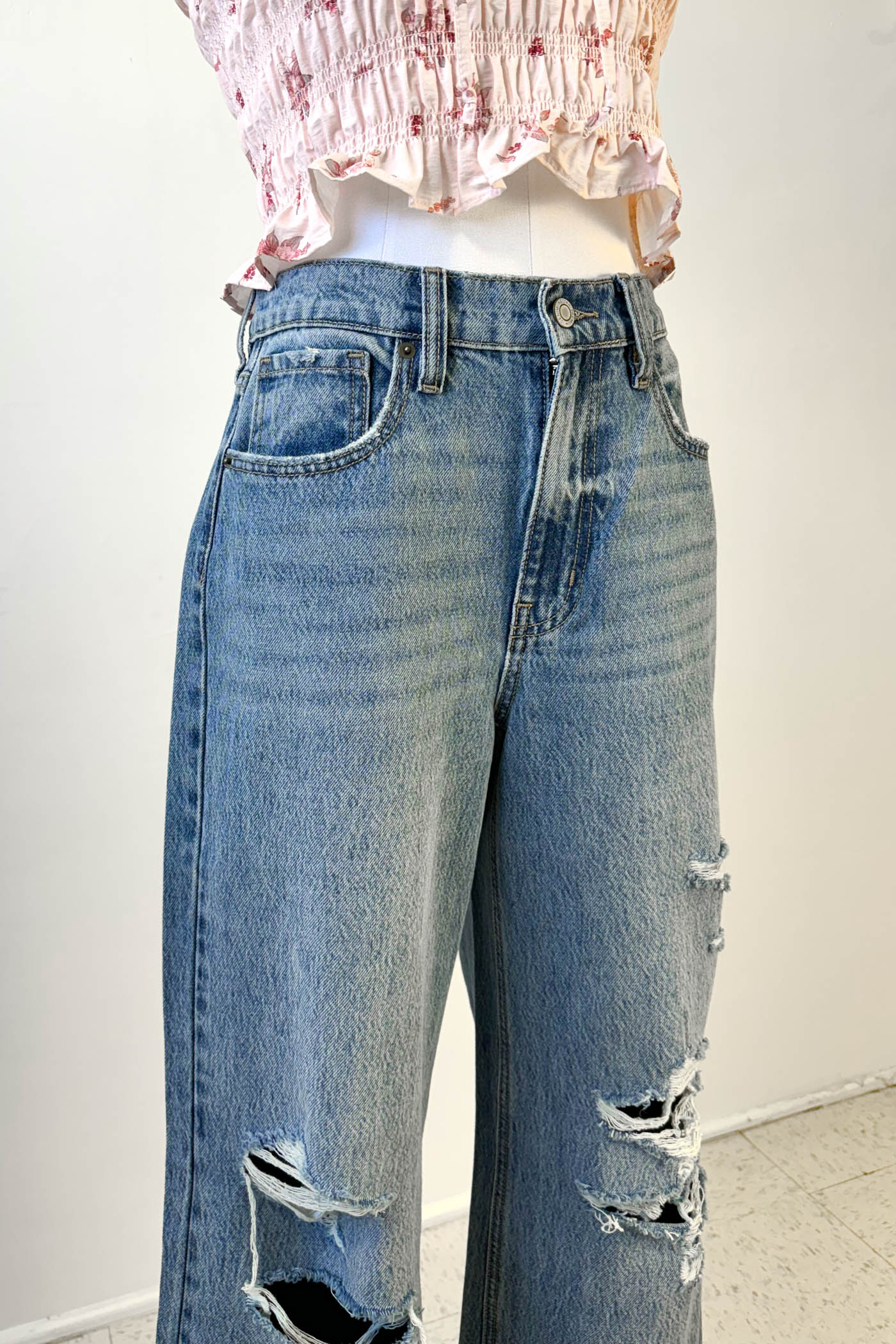 Person wearing ripped blue jeans and a pink top against a white background