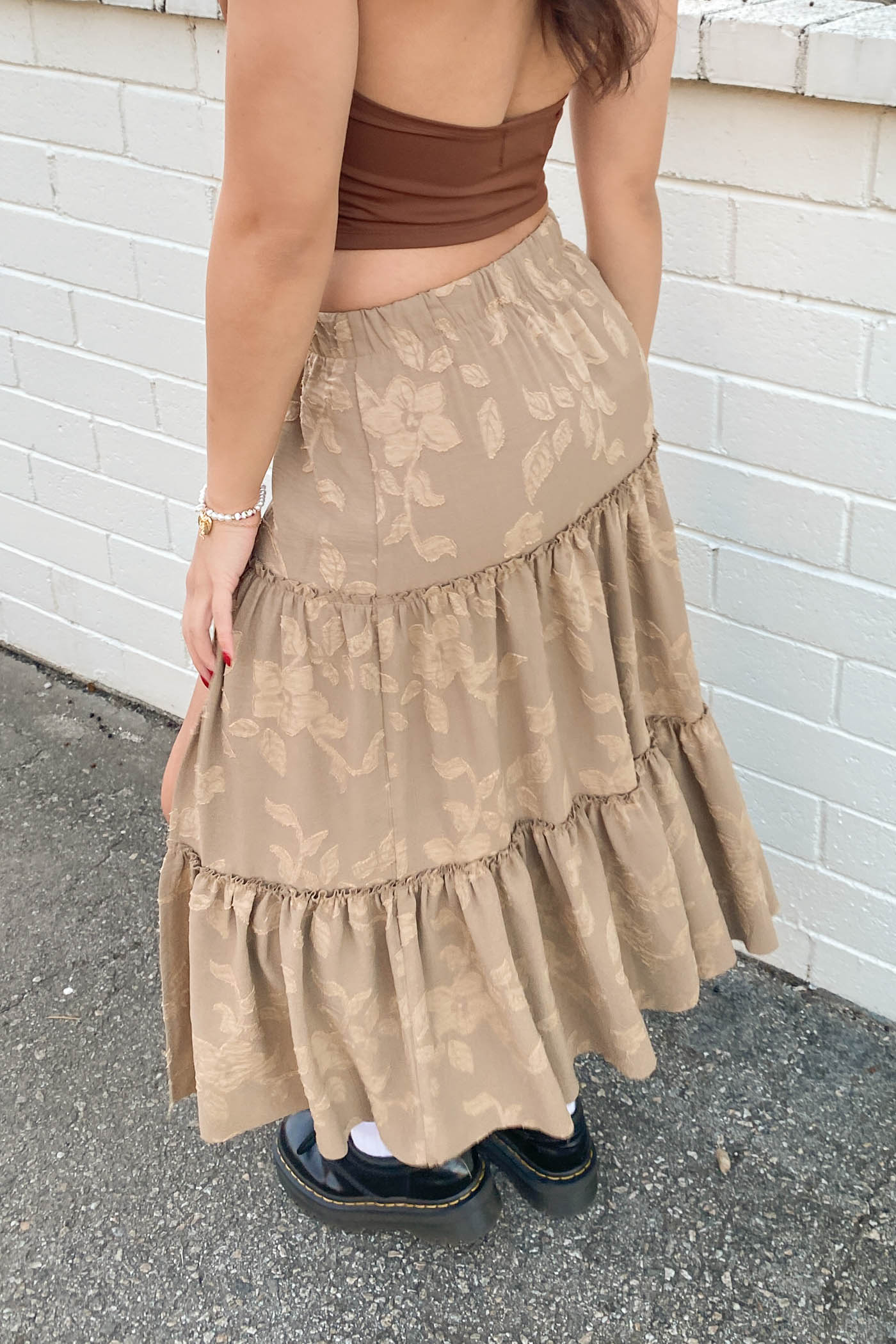 Person wearing a brown tiered skirt against a white brick wall.