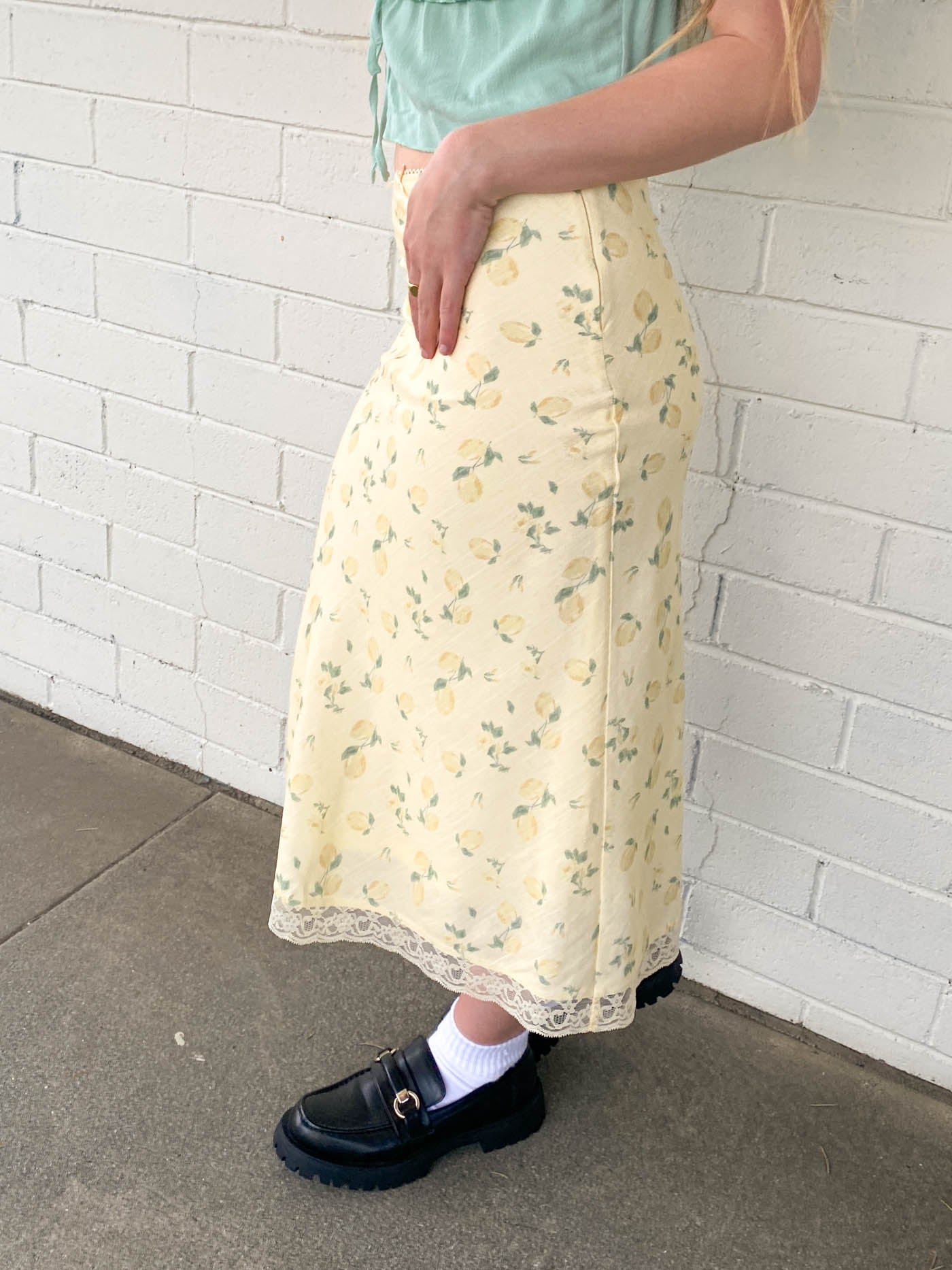 Person wearing a yellow floral skirt with a white brick wall background