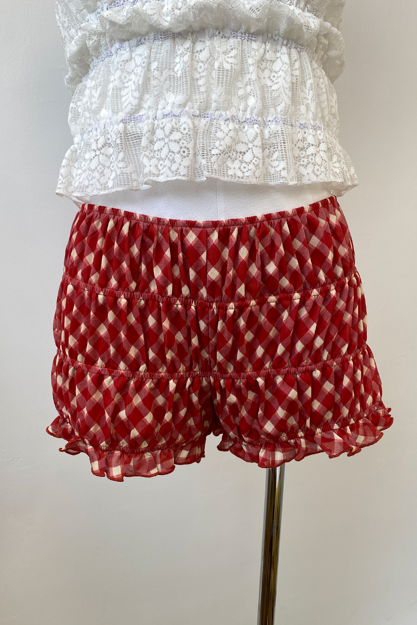 Bloomer shorts with a red and white plaid pattern and ruffled hem, displayed on a mannequin.