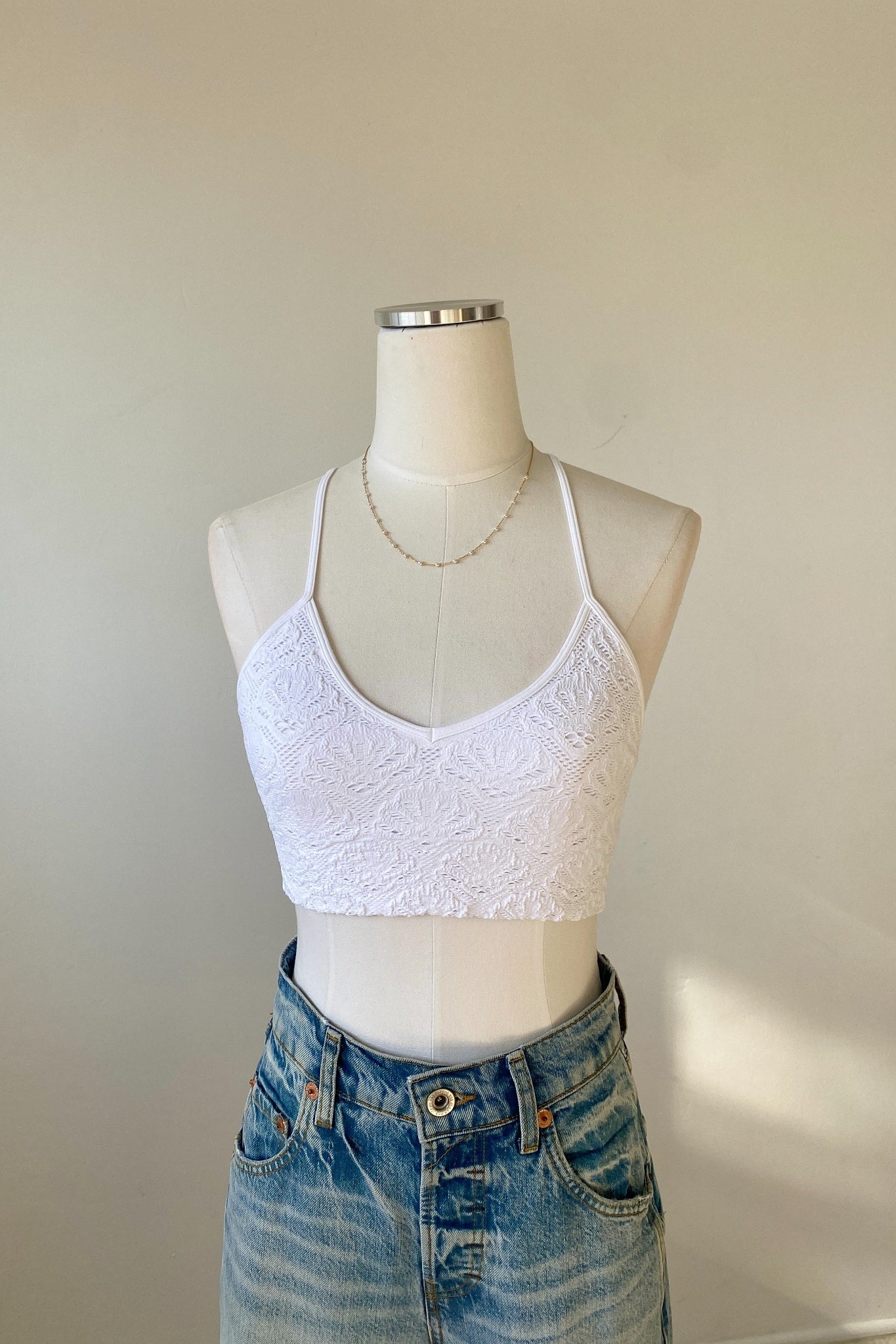 White lace crop top on a mannequin with blue jeans against a plain background