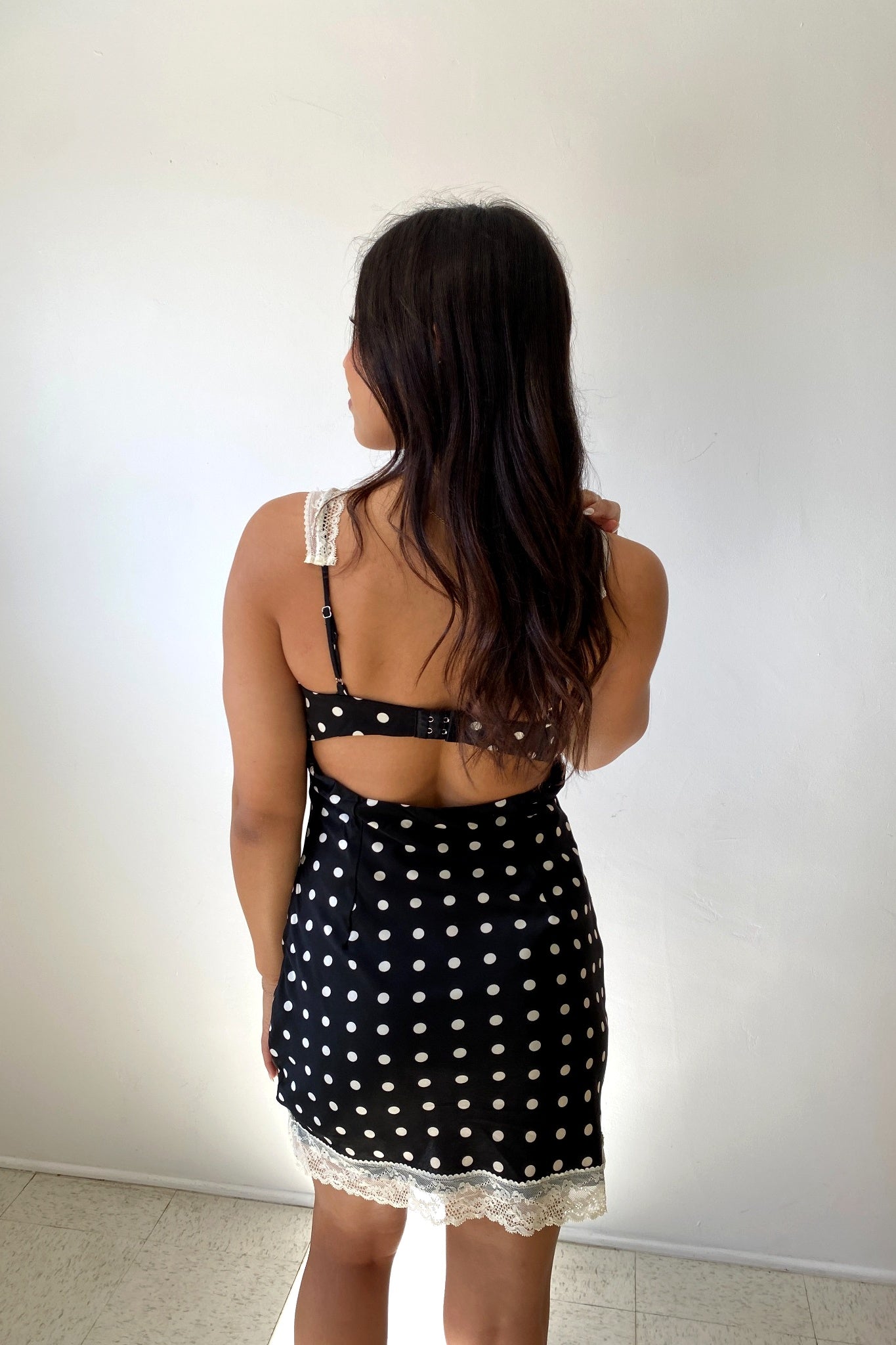 Woman wearing a black polka dot dress with lace trim against a white background