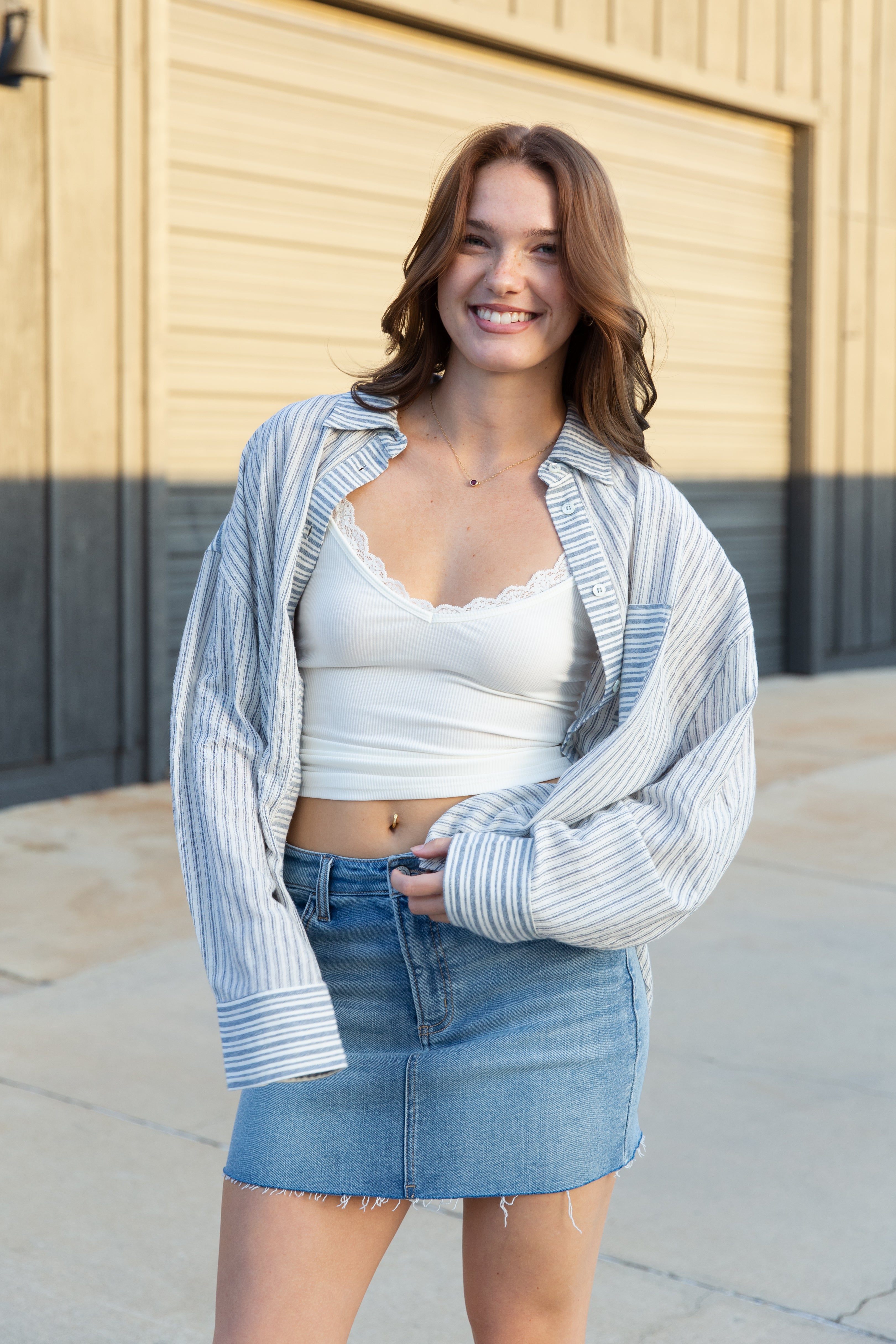 Woman wearing a white crop top and denim skirt with a striped cardigan outdoors.