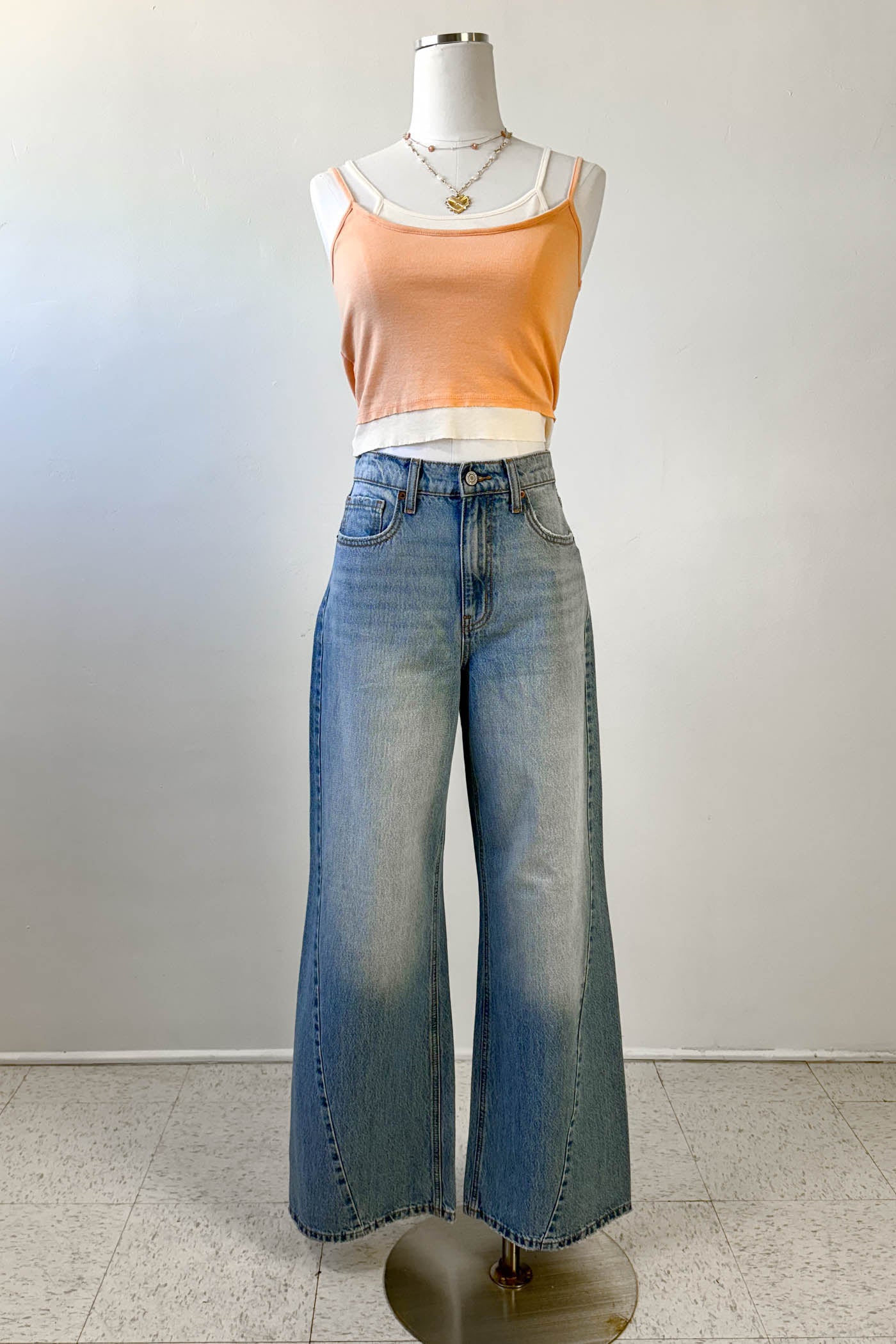 Mannequin wearing a peach tank top and blue jeans against a white background