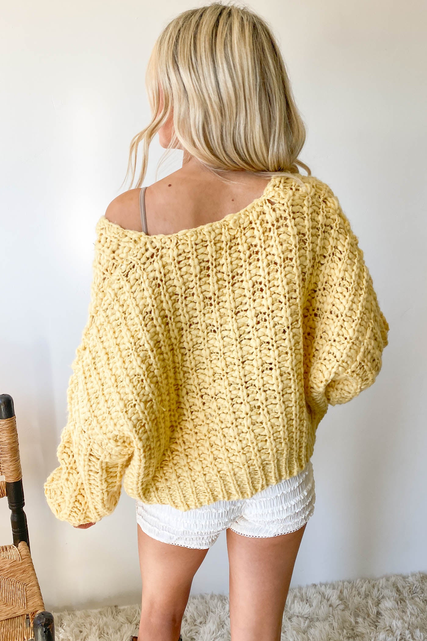 Person wearing a yellow crochet sweater and white shorts against a plain background
