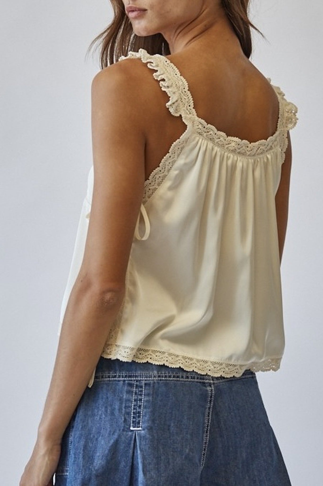Woman wearing a beige lace-trimmed top and blue jeans against a white background