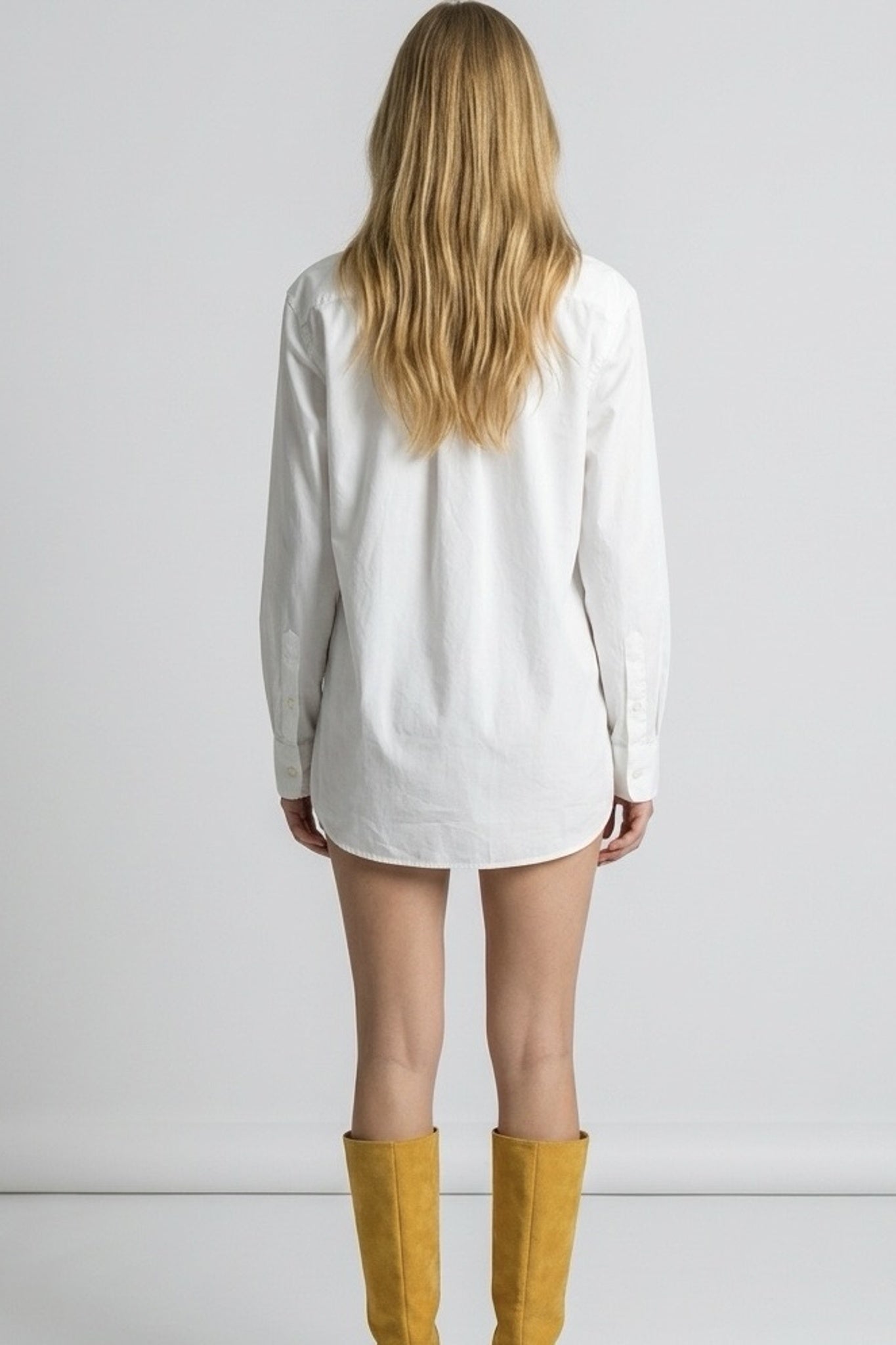 Person wearing a white oversized shirt and yellow boots on a plain background
