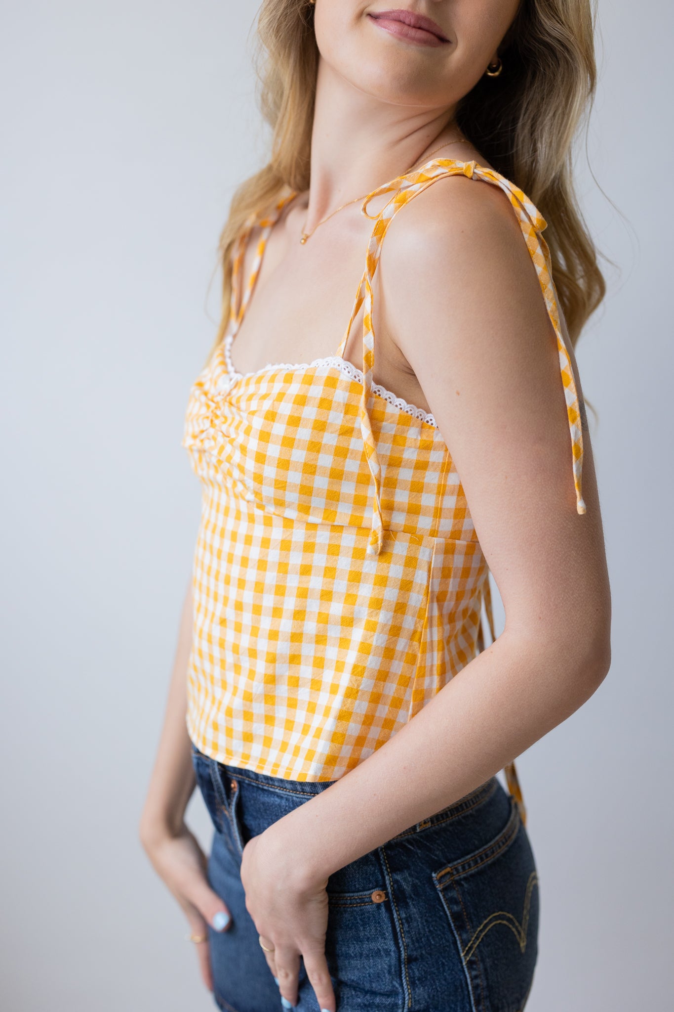 Woman wearing a yellow and white checkered top with blue jeans on a plain background