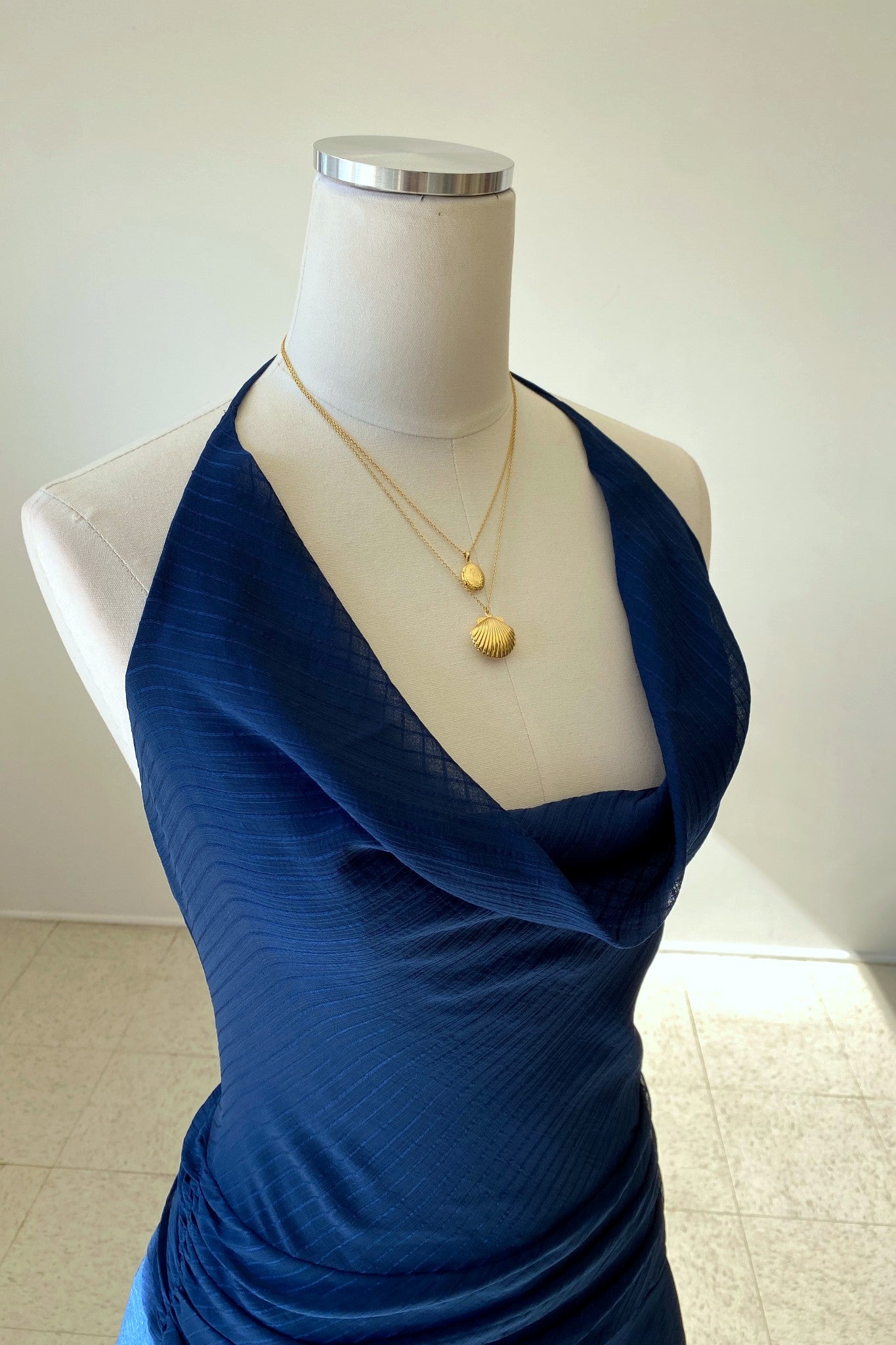 Mannequin wearing a blue dress with gold necklaces on a plain background