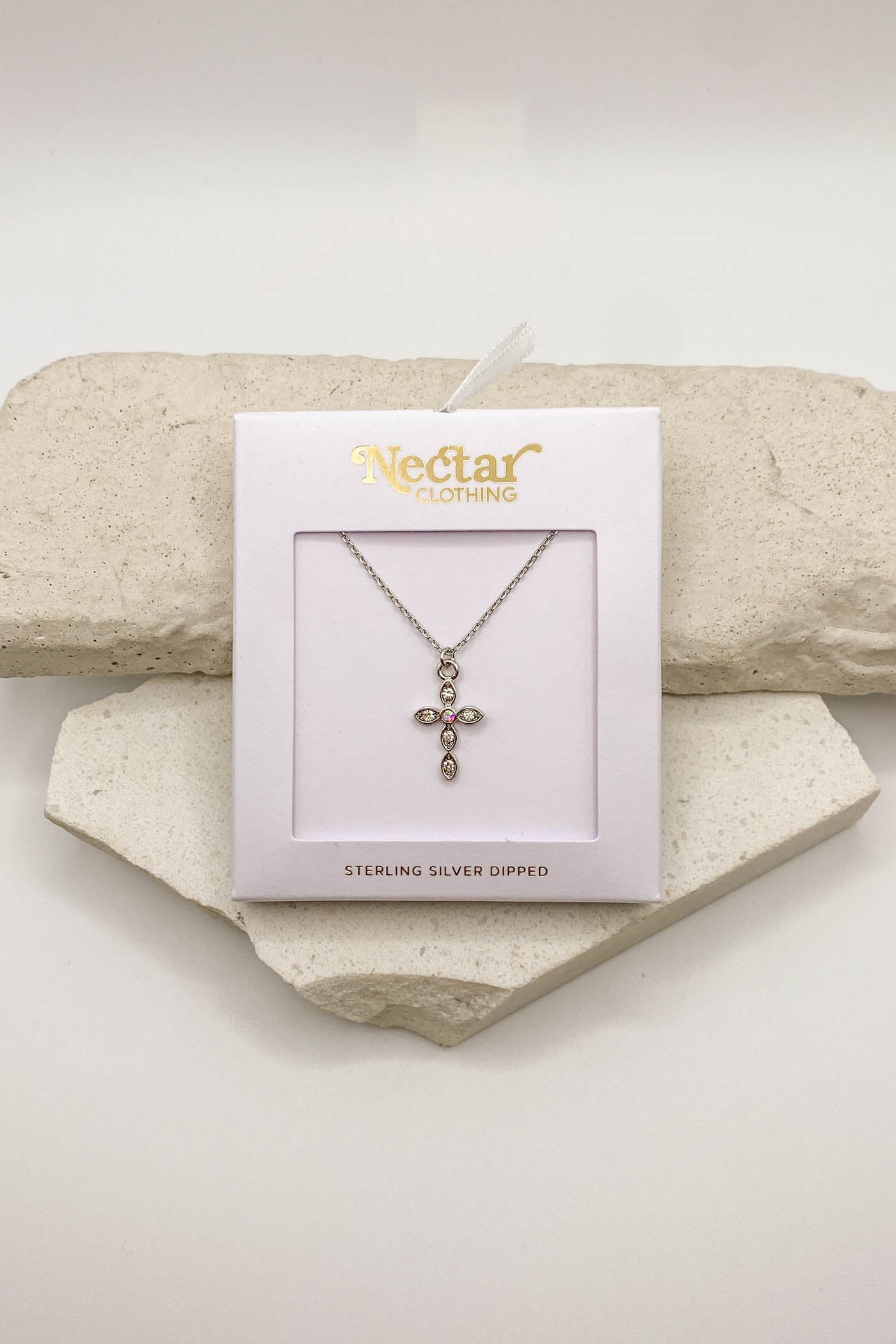 Necklace with cross pendant on a Nectar Clothing card, displayed on a stone surface.