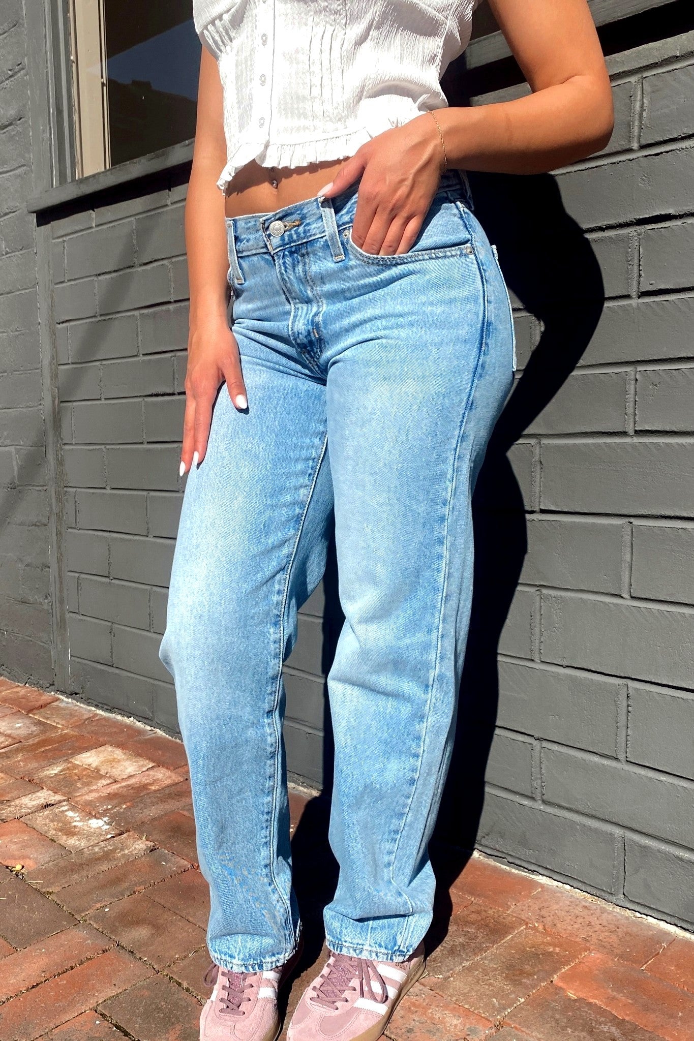 Person wearing light blue jeans and a white top against a gray brick wall.