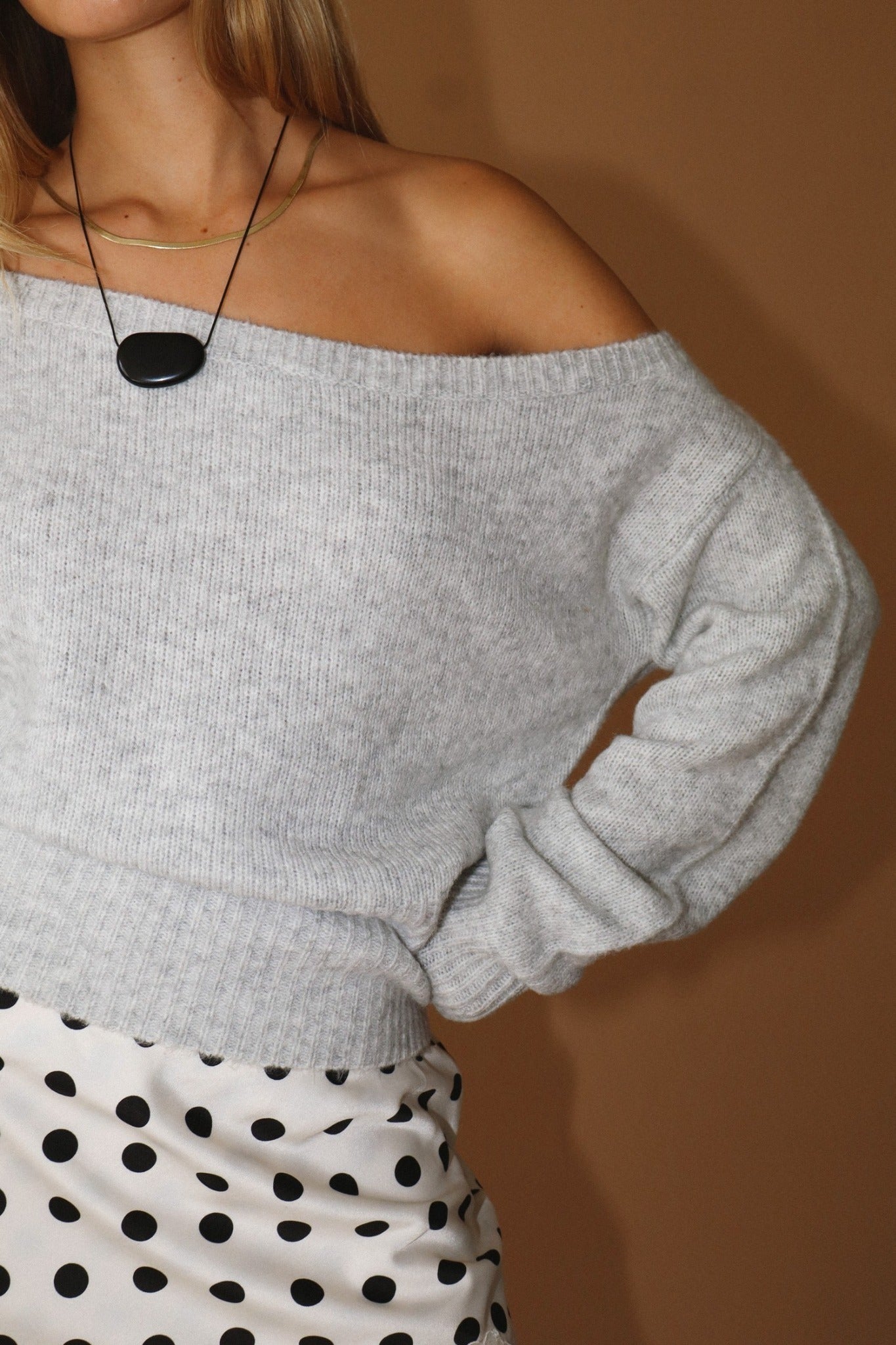 Gray off-shoulder sweater worn by a person with a brown background