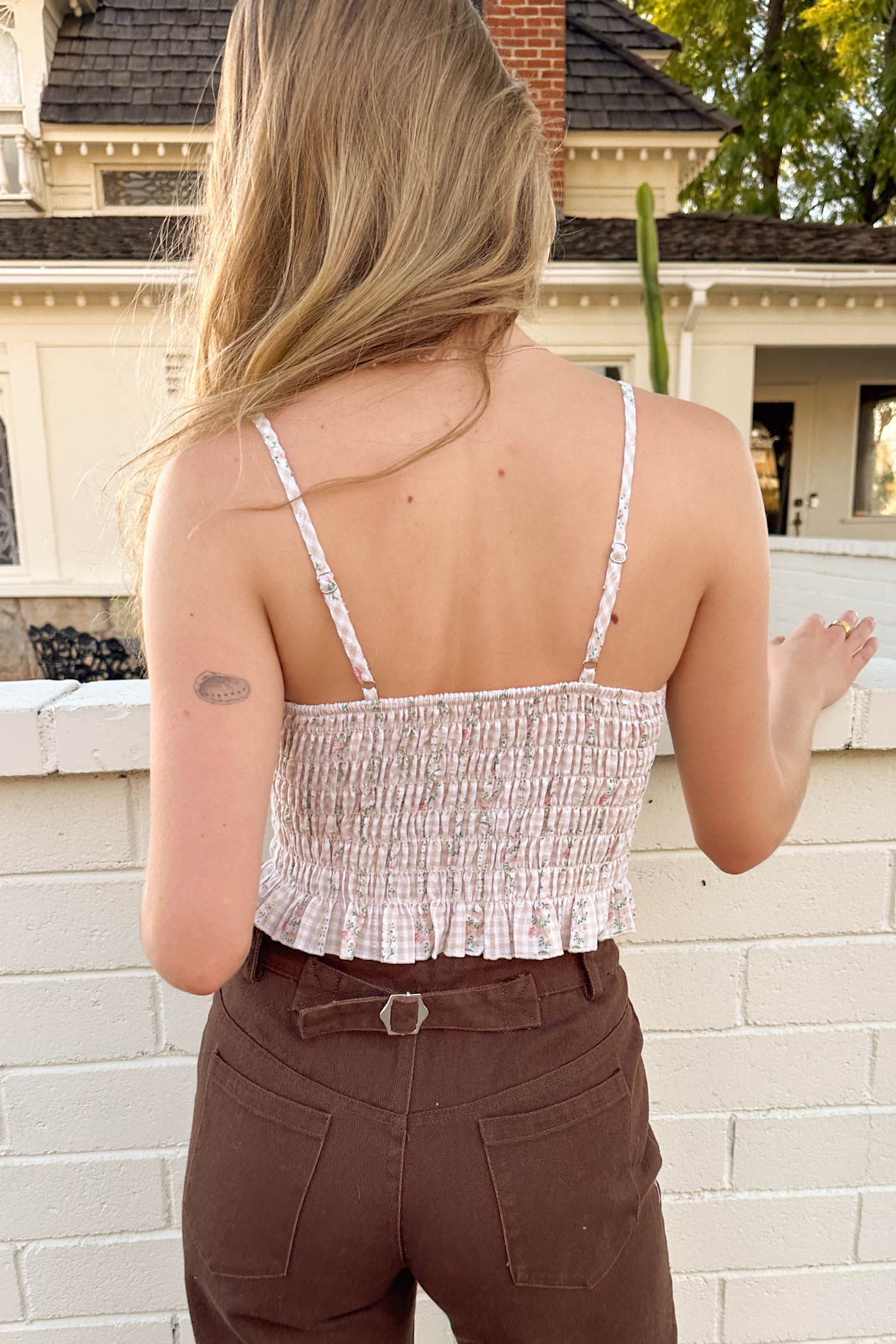 Person wearing a patterned top and brown pants standing in front of a white brick wall.