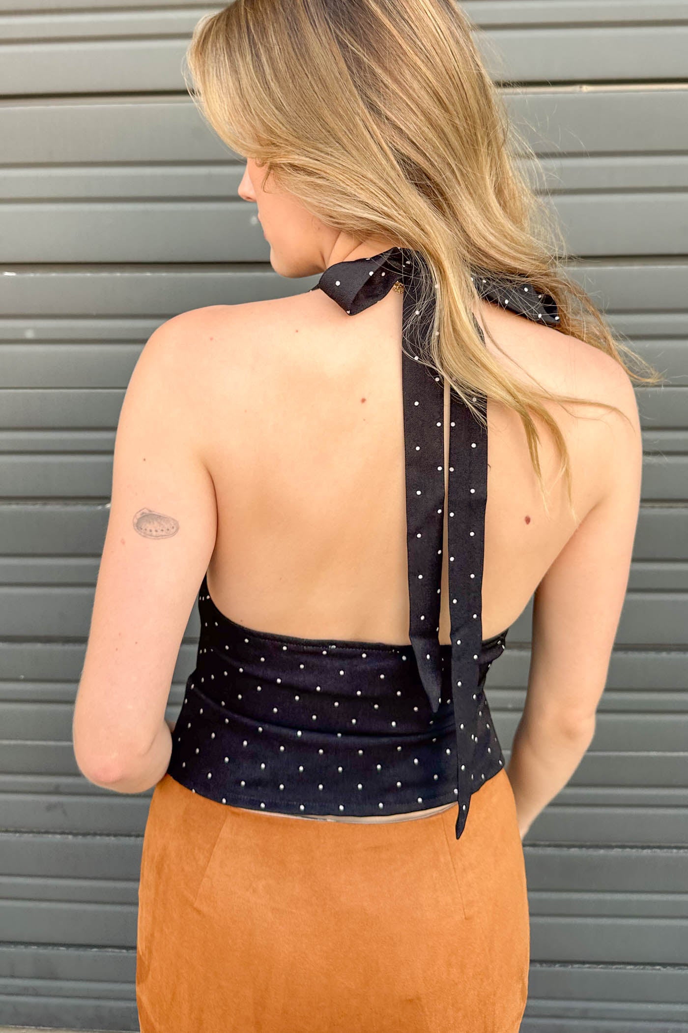 Woman wearing a black polka dot halter top with a gray background