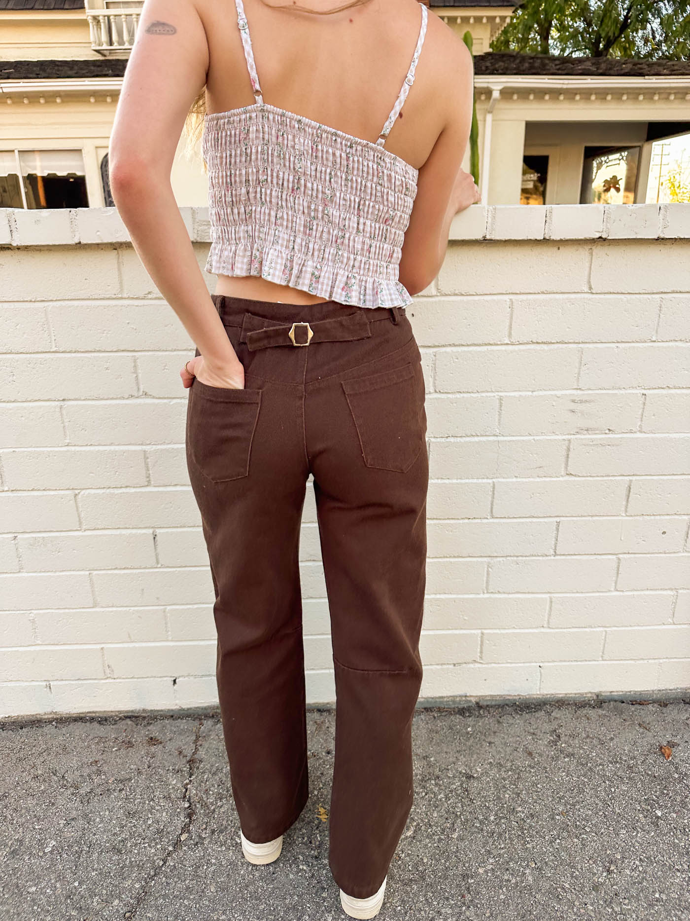 Person wearing a patterned crop top and brown pants standing against a white brick wall.