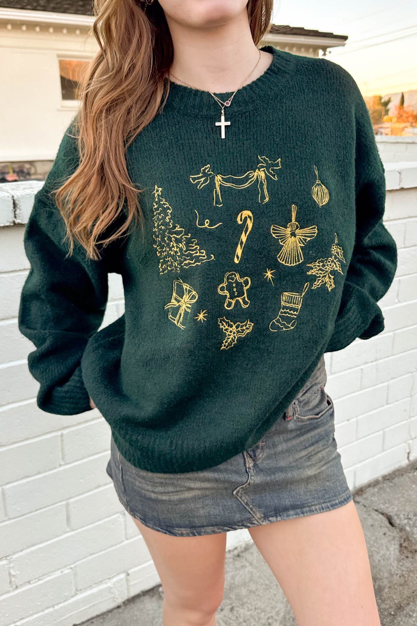 Person wearing a green sweater with gold designs against a white brick wall.