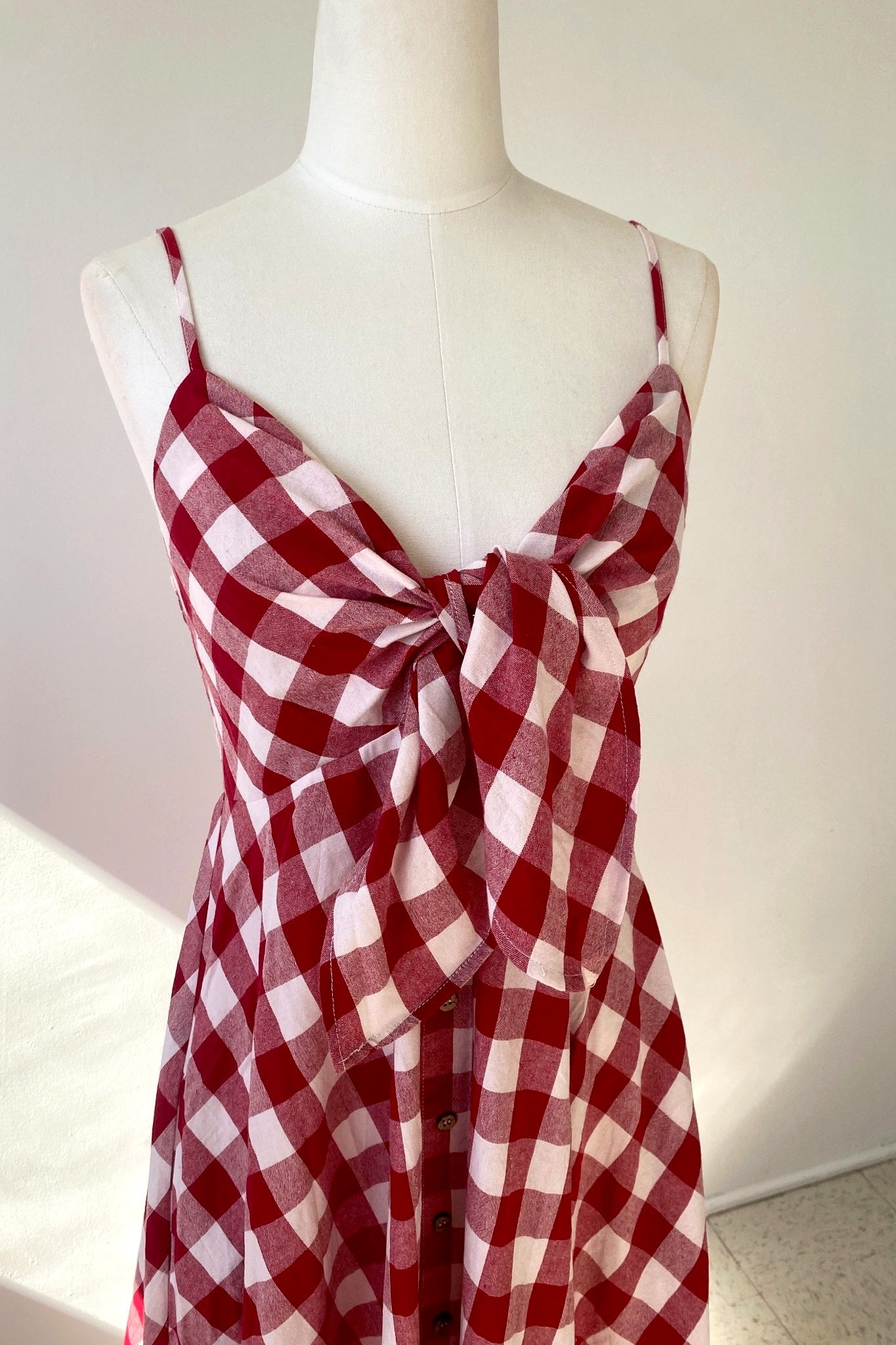 Red and white checkered dress on a mannequin against a plain background
