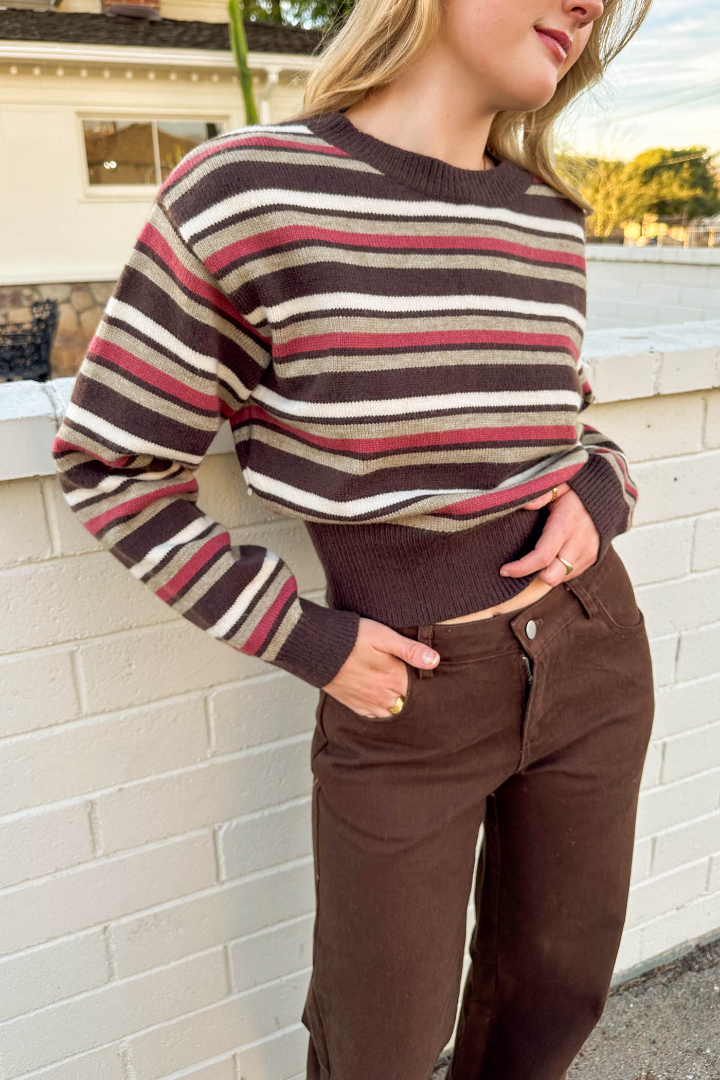 Person wearing a striped sweater and brown pants against a white brick wall.