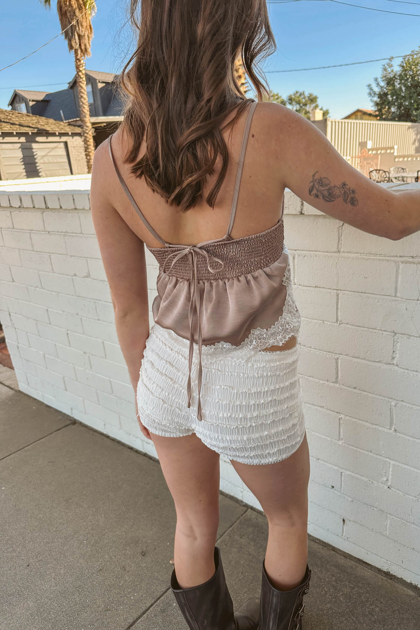 Person wearing a brown top and white shorts standing against a white brick wall.