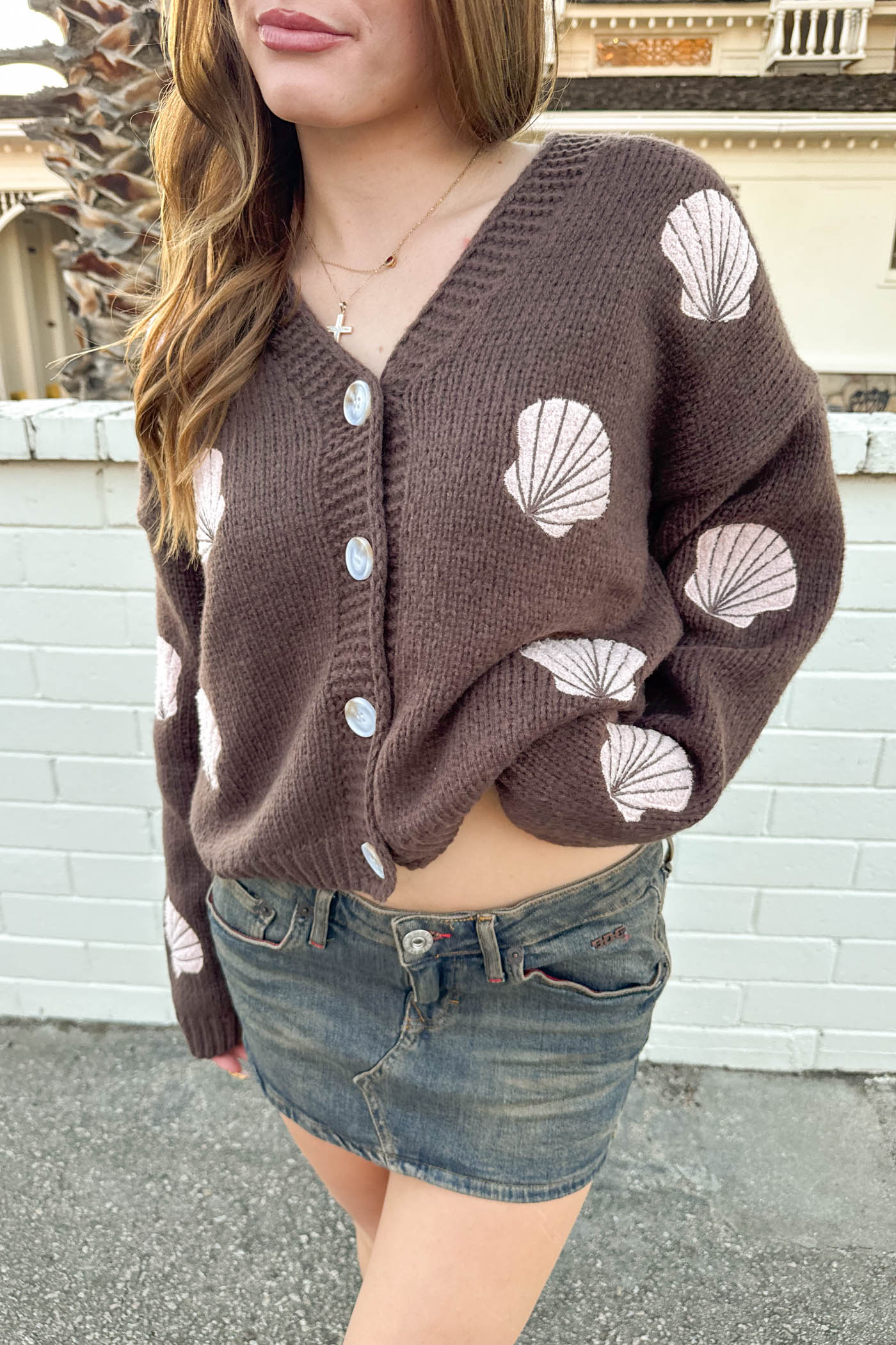 Person wearing a brown cardigan with white shell patterns and denim shorts.