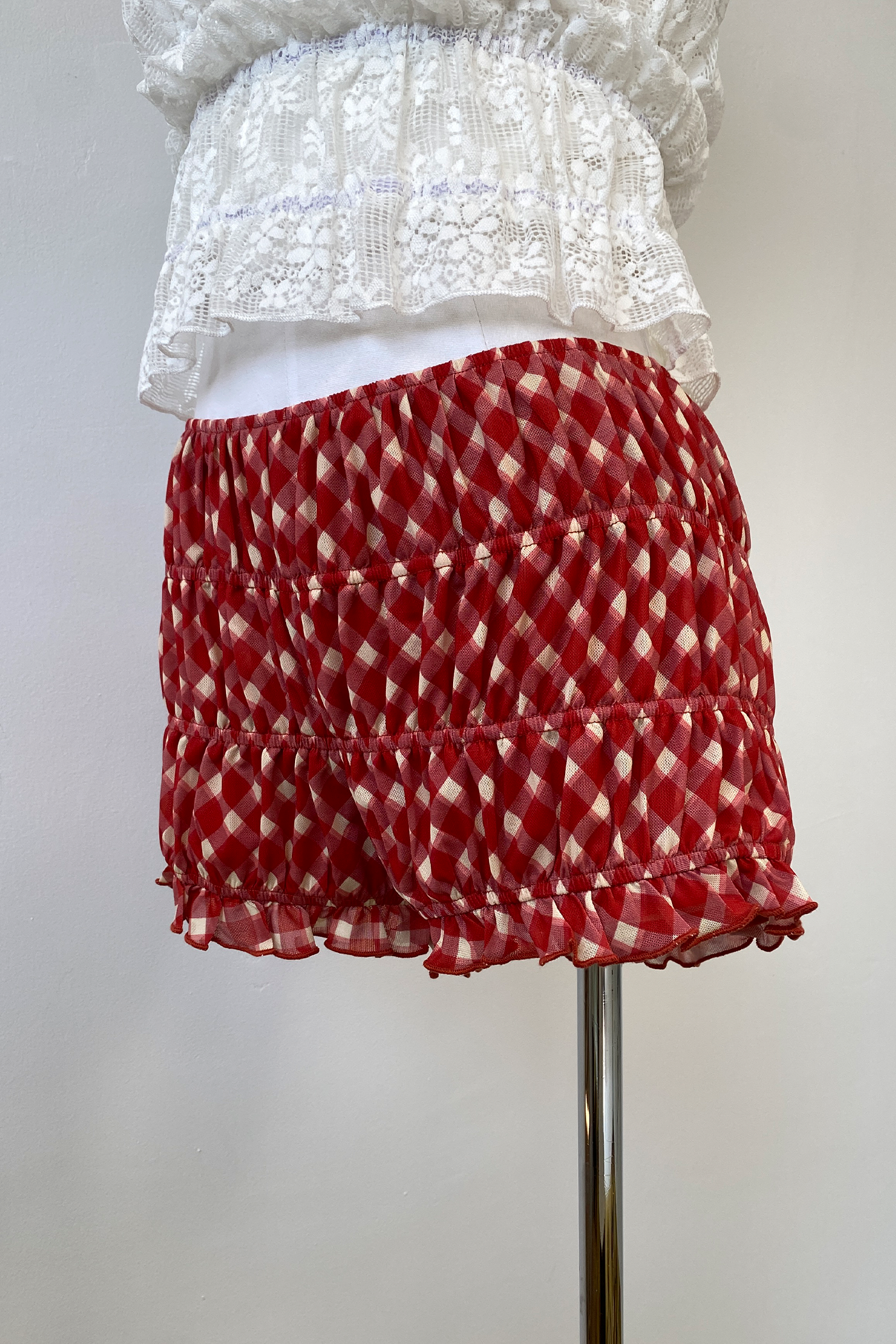 Red and white plaid patterned bloomers with a ruffled hem and elastic waistband, displayed on a mannequin wearing a white lace top.