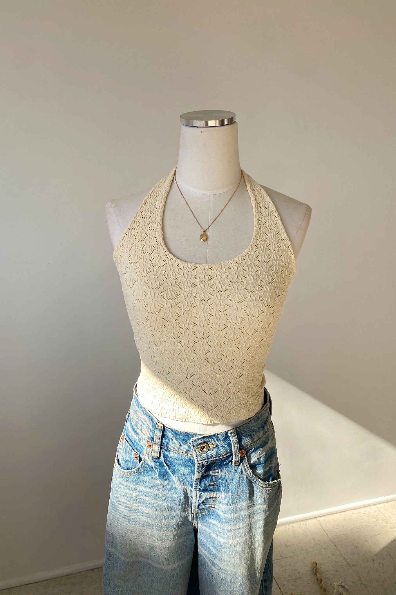 Mannequin wearing a beige lace top and blue jeans against a plain background