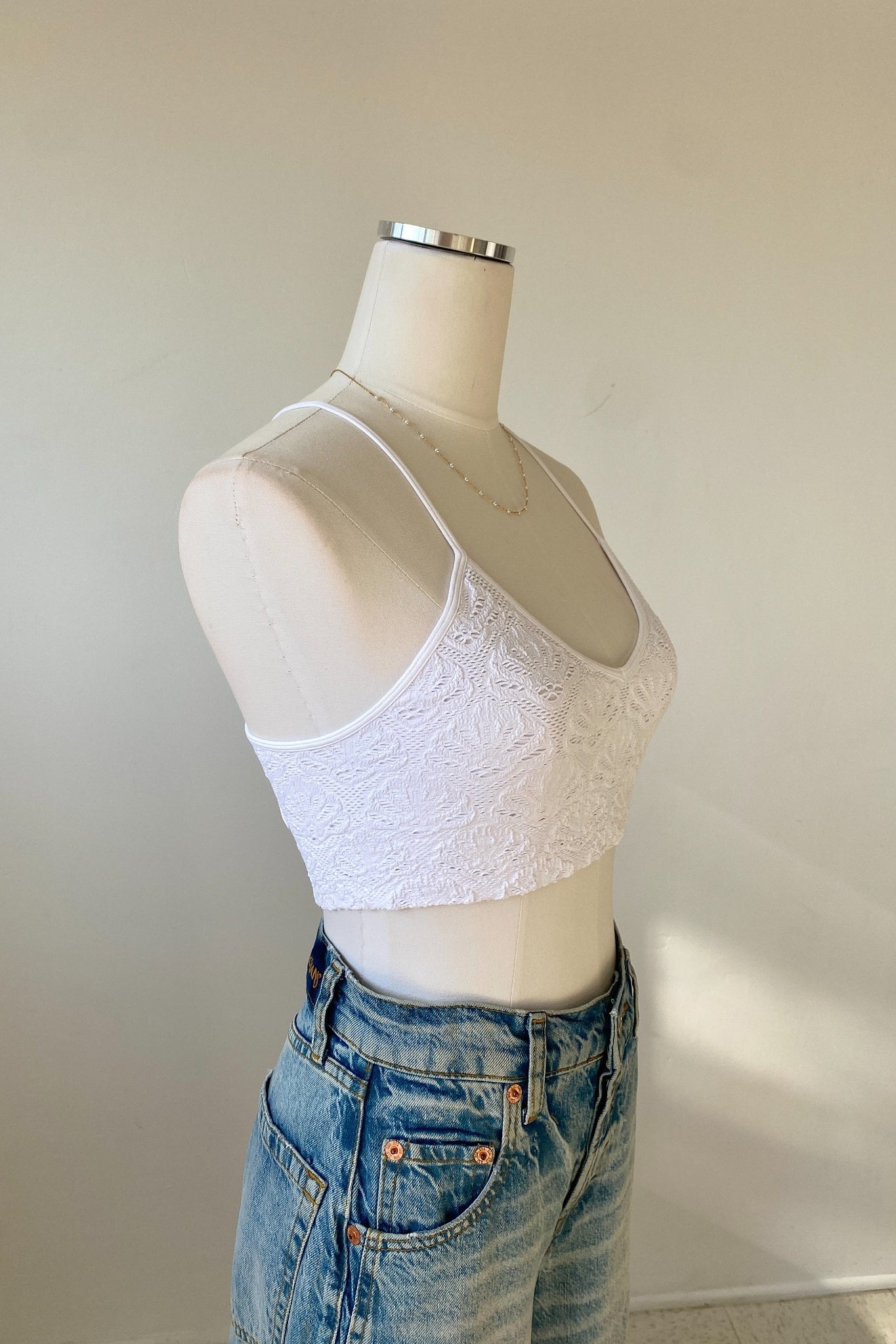 Mannequin wearing a white lace crop top and blue jeans against a plain background