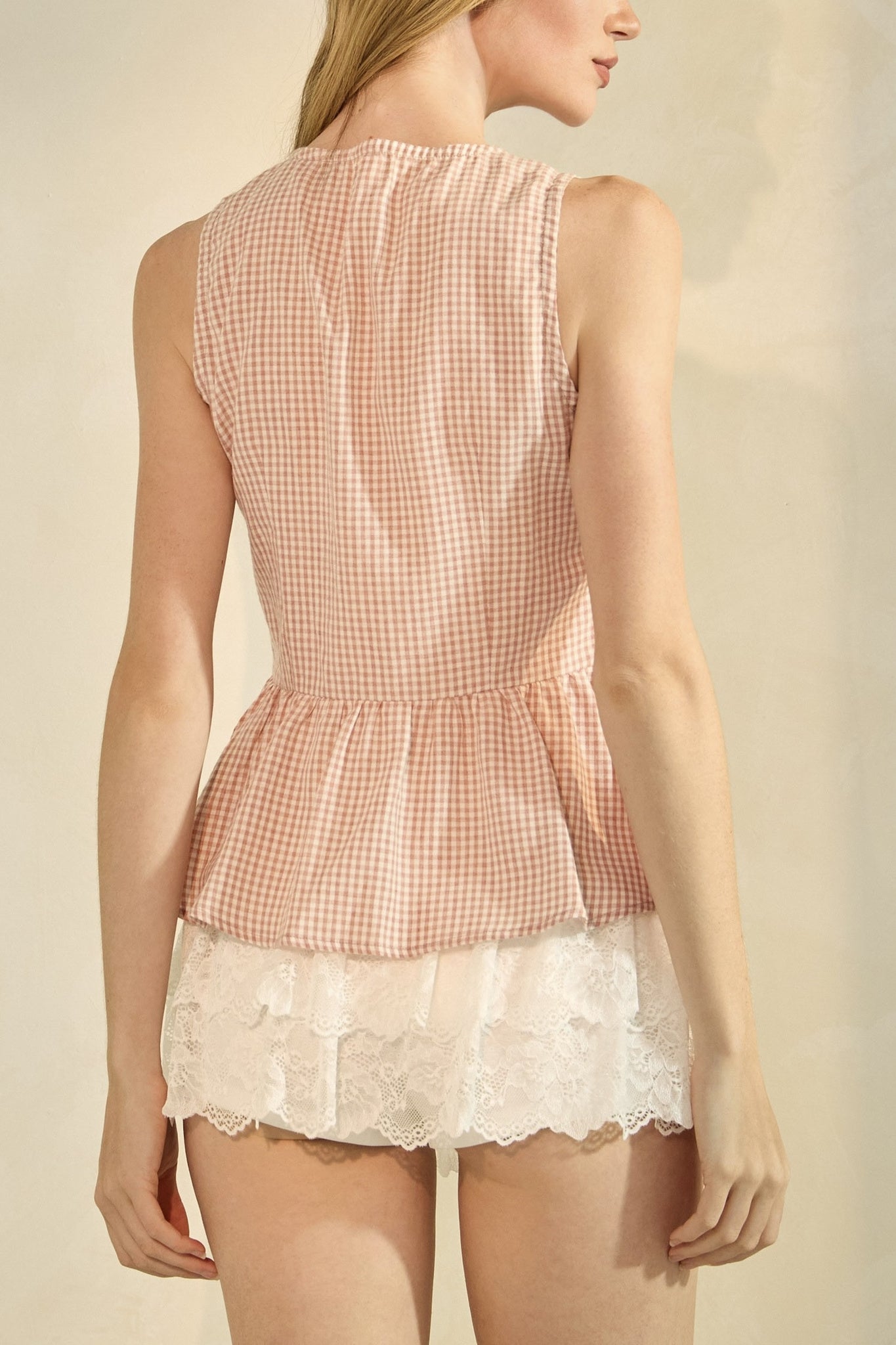 Woman wearing a pink checkered top and white lace shorts on a beige background