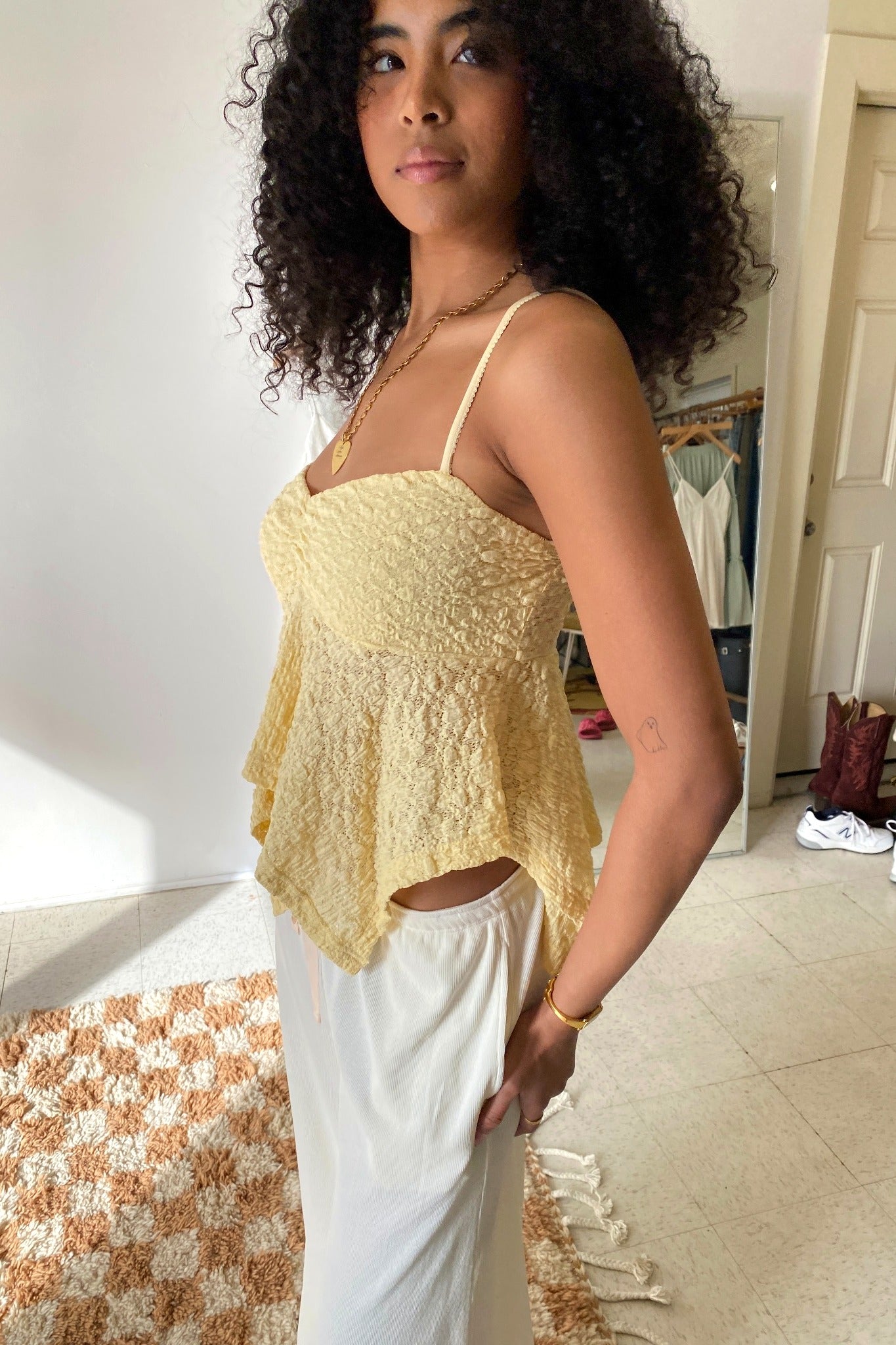 Woman wearing a yellow lace top and white pants in a room with a checkered rug.