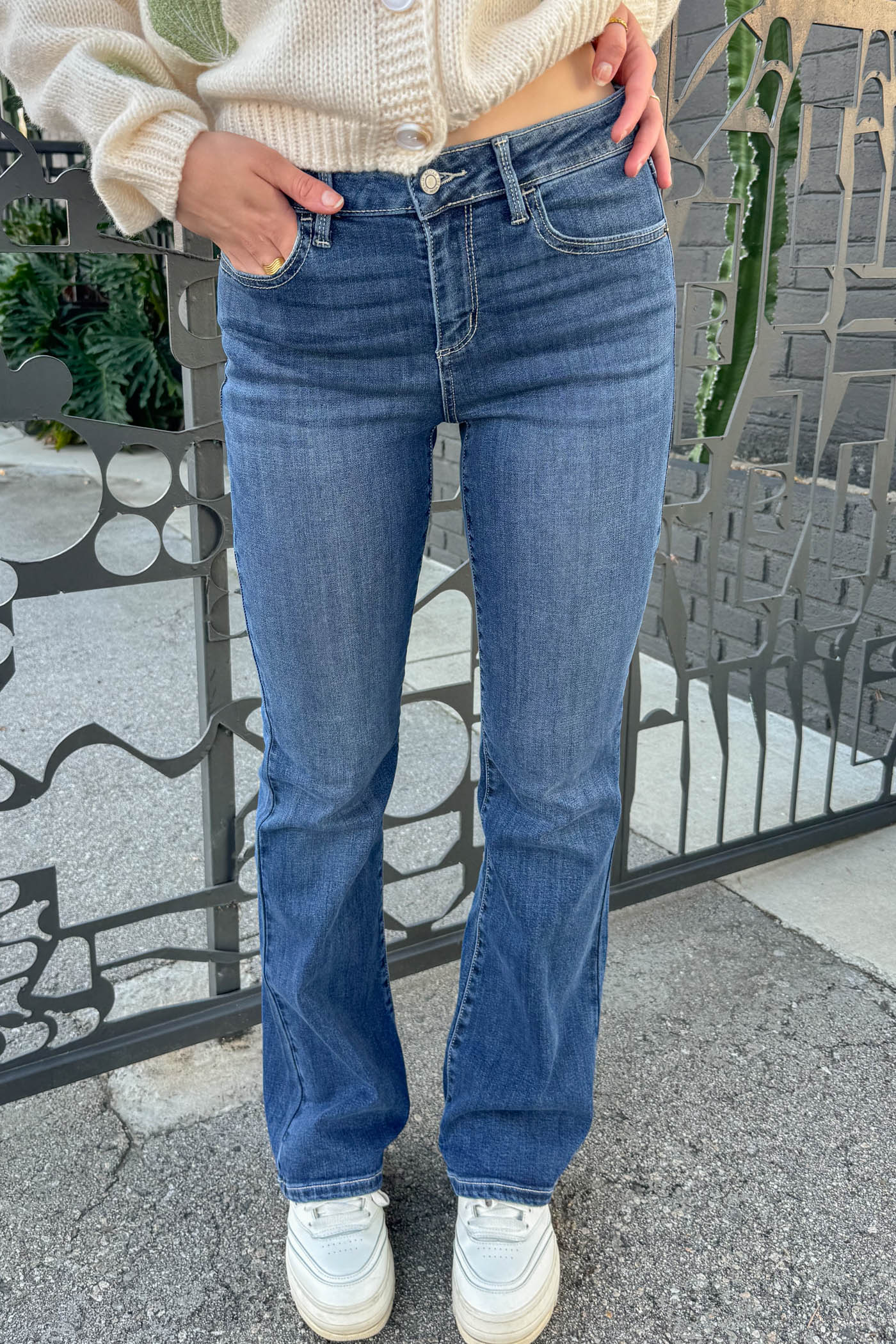 Person wearing blue jeans and a cream sweater standing against a decorative stone wall.