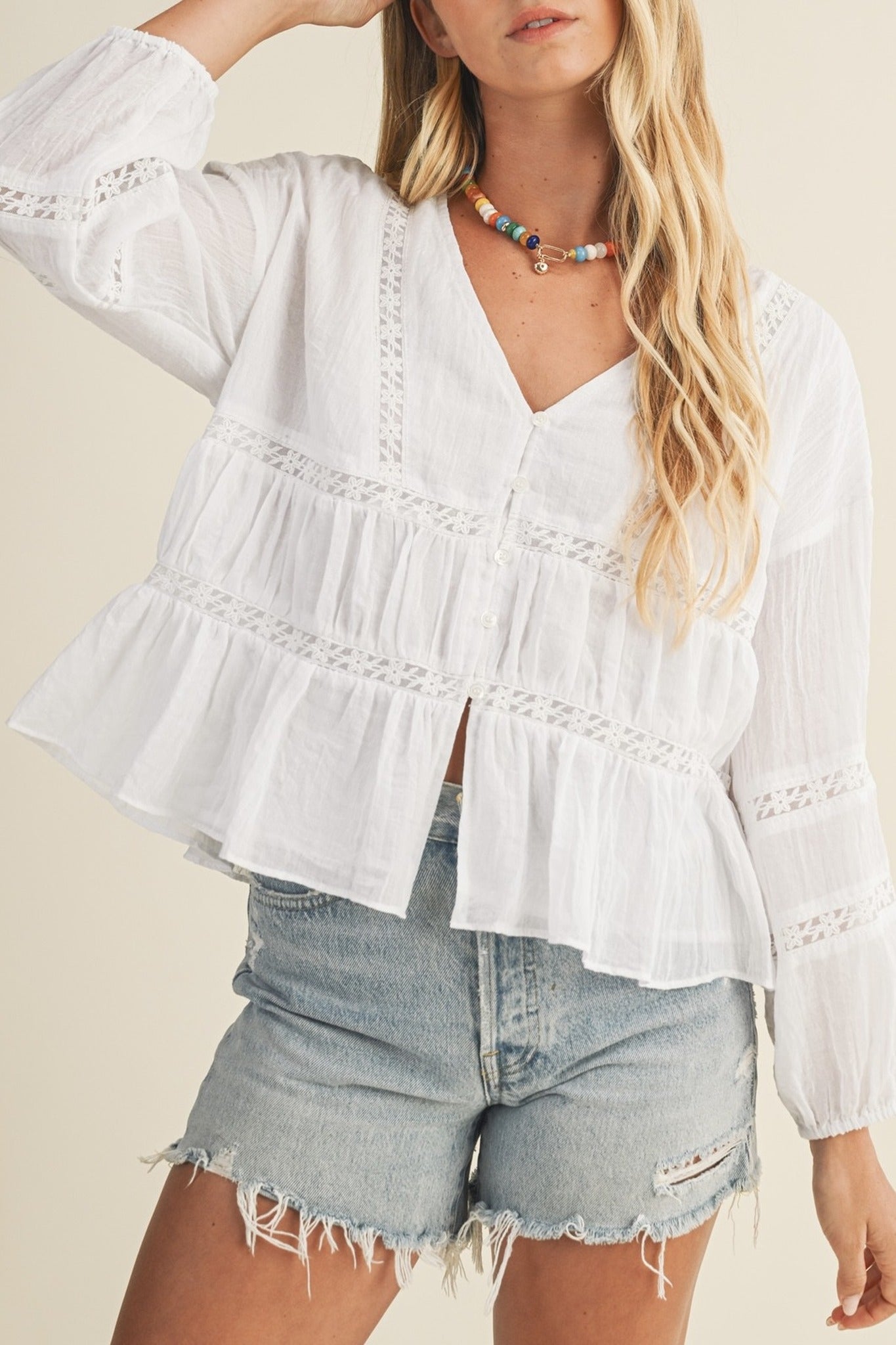 Woman wearing a white blouse with ruffled details and denim shorts on a plain background