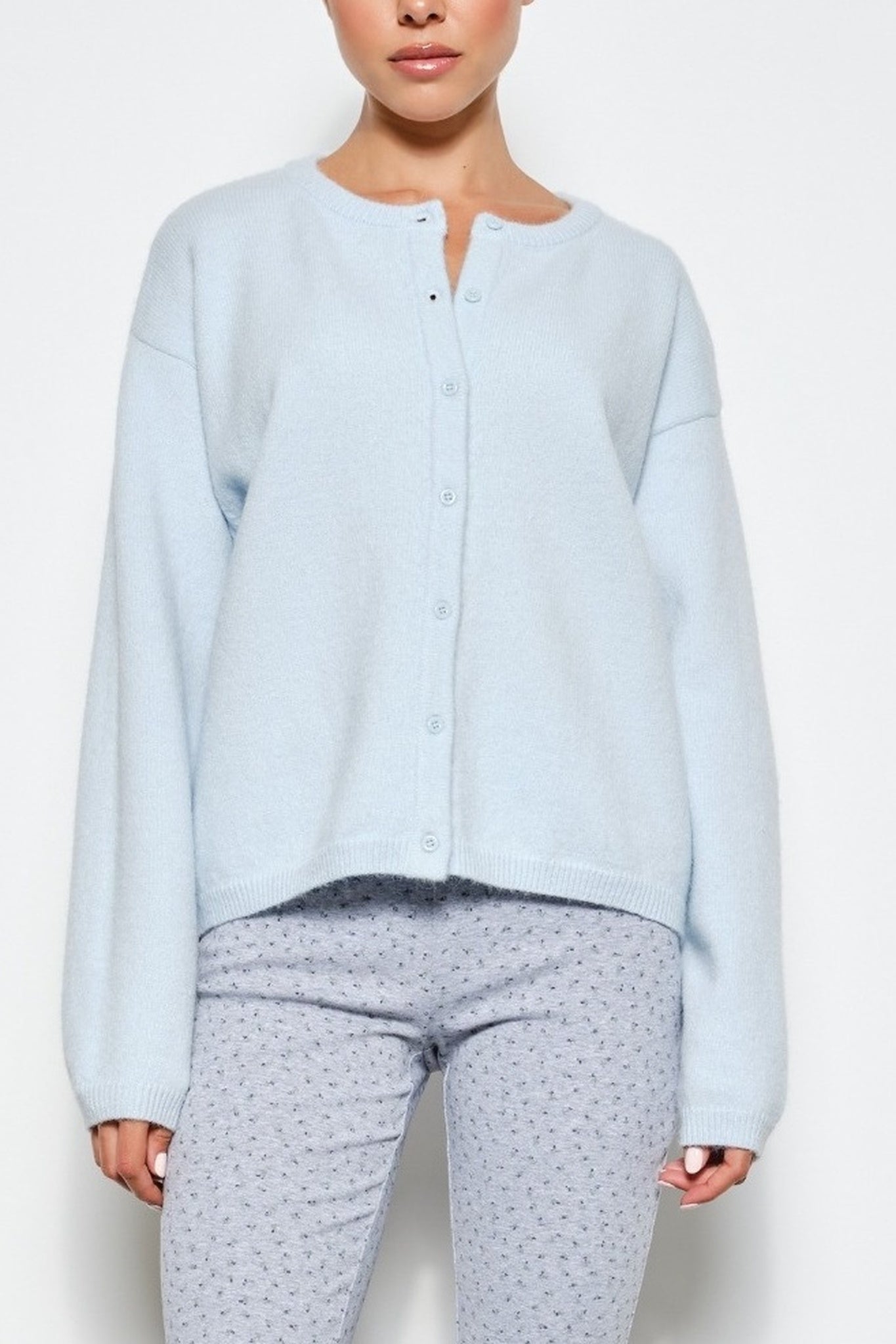 A woman wearing a light blue button-front cardigan and light gray patterned pajama pants against a plain white background.