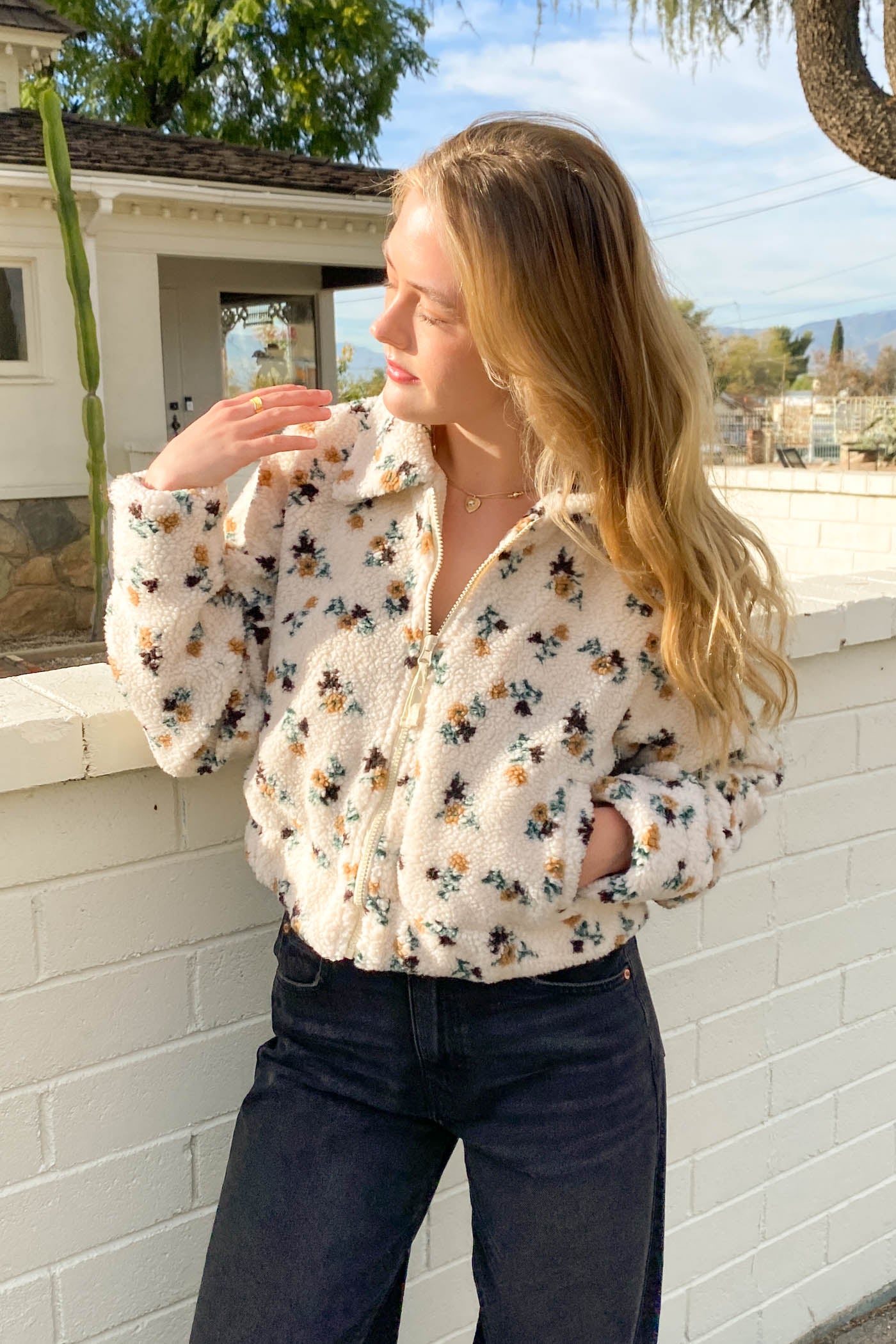 Woman wearing a floral blouse and dark jeans standing outdoors.