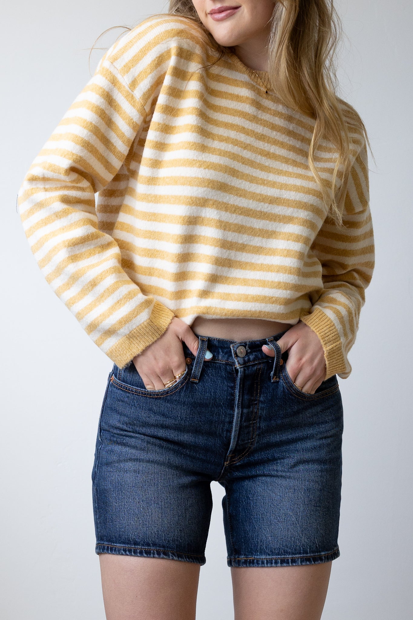 Person wearing a yellow and white striped sweater and blue denim shorts on a plain background