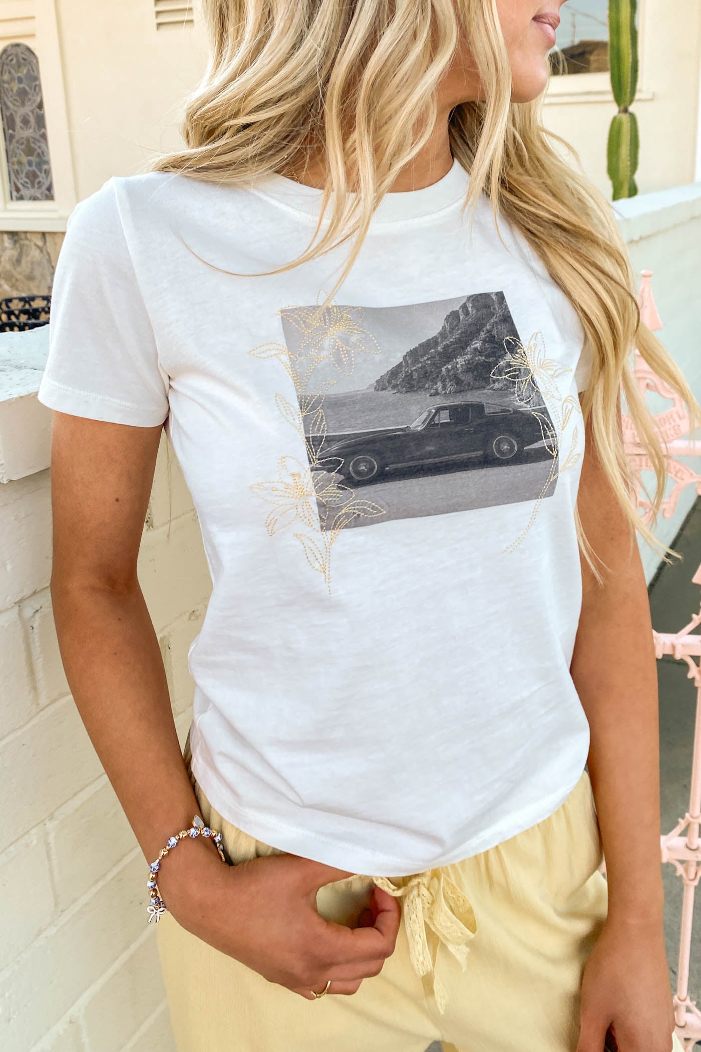 Person wearing a white t-shirt with a graphic design, standing in an outdoor setting.