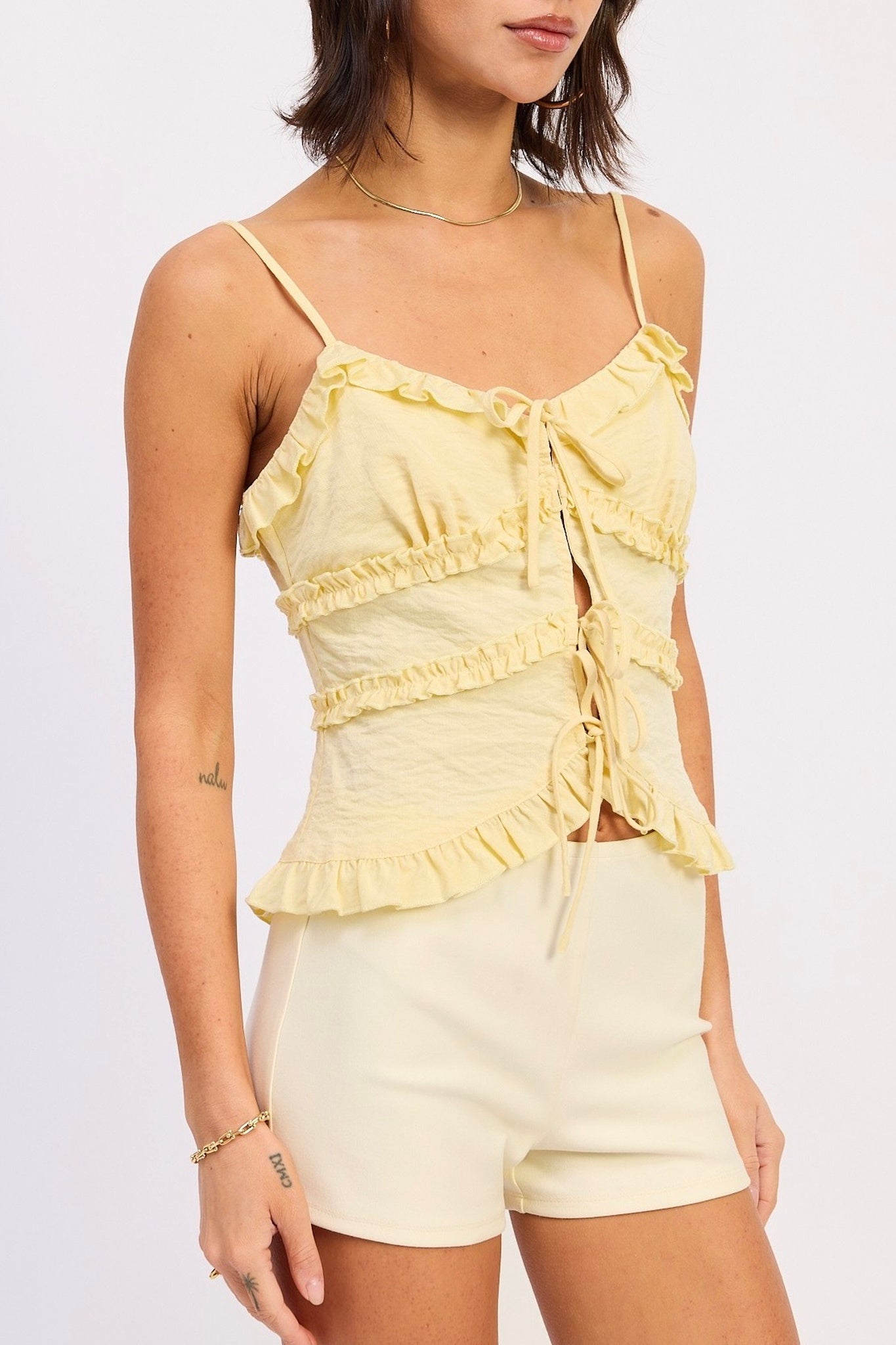 Woman wearing a yellow ruffled top and shorts on a light gray background