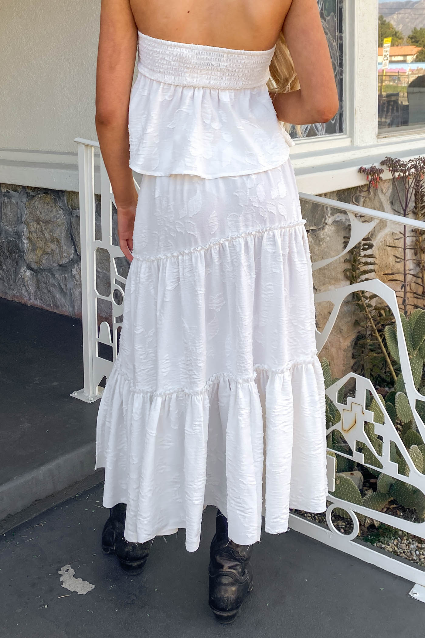 Person wearing a white dress with ruffled layers on a patio.