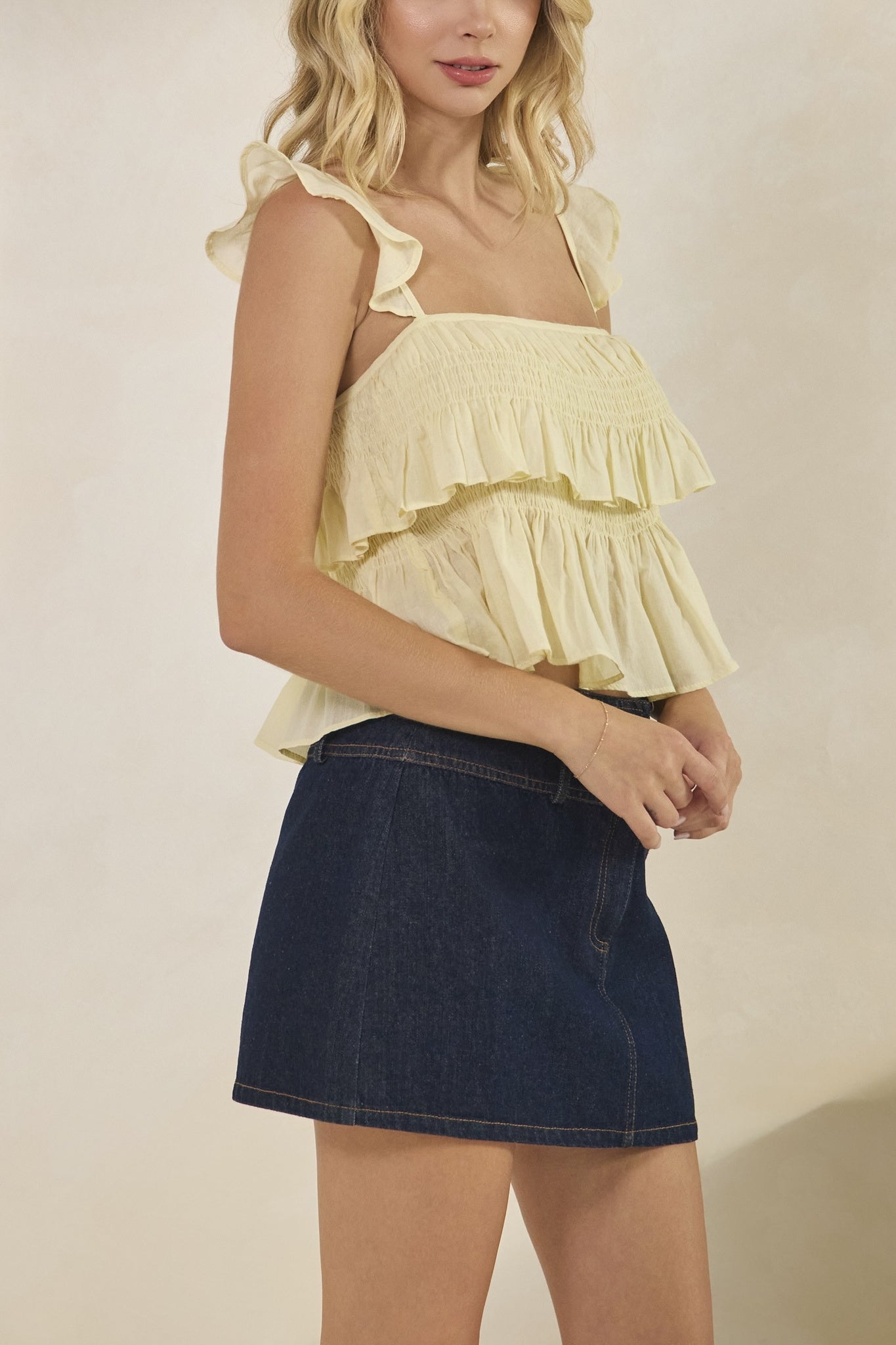 Woman wearing a yellow ruffled top and denim skirt against a plain background