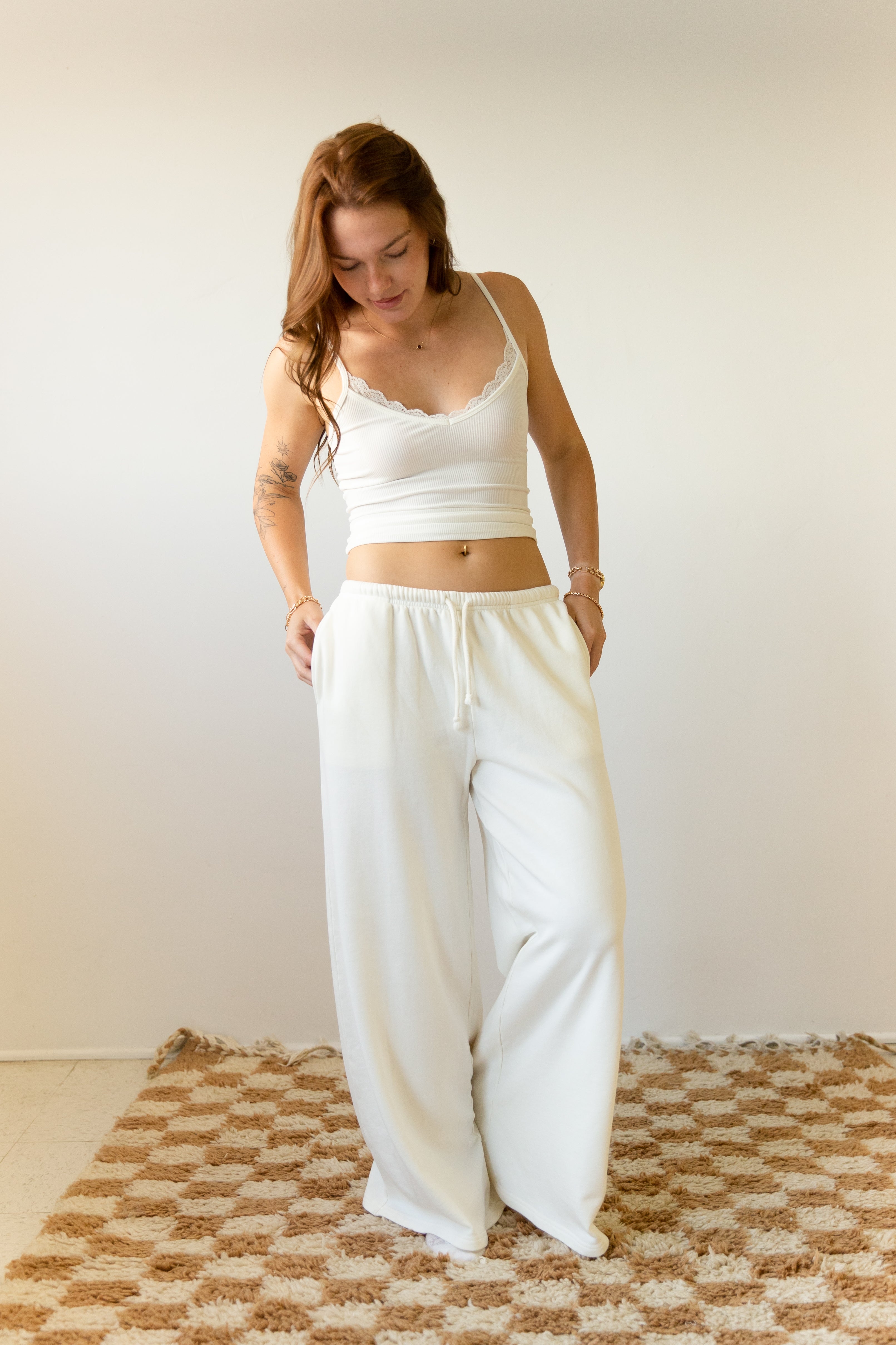 Woman wearing a white tank top and wide-leg pants standing on a textured rug.