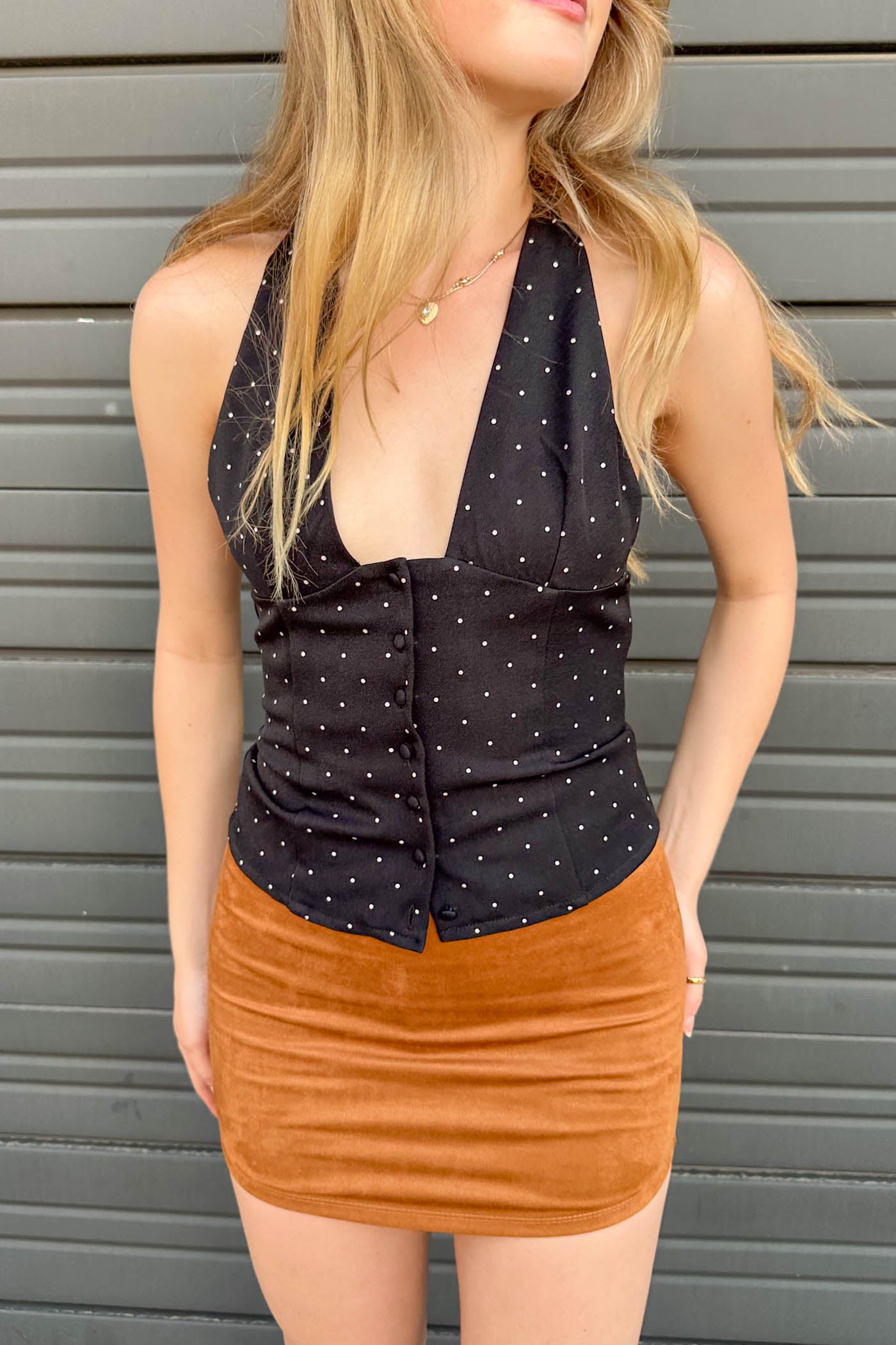 Woman wearing a black polka dot top and brown skirt against a gray background