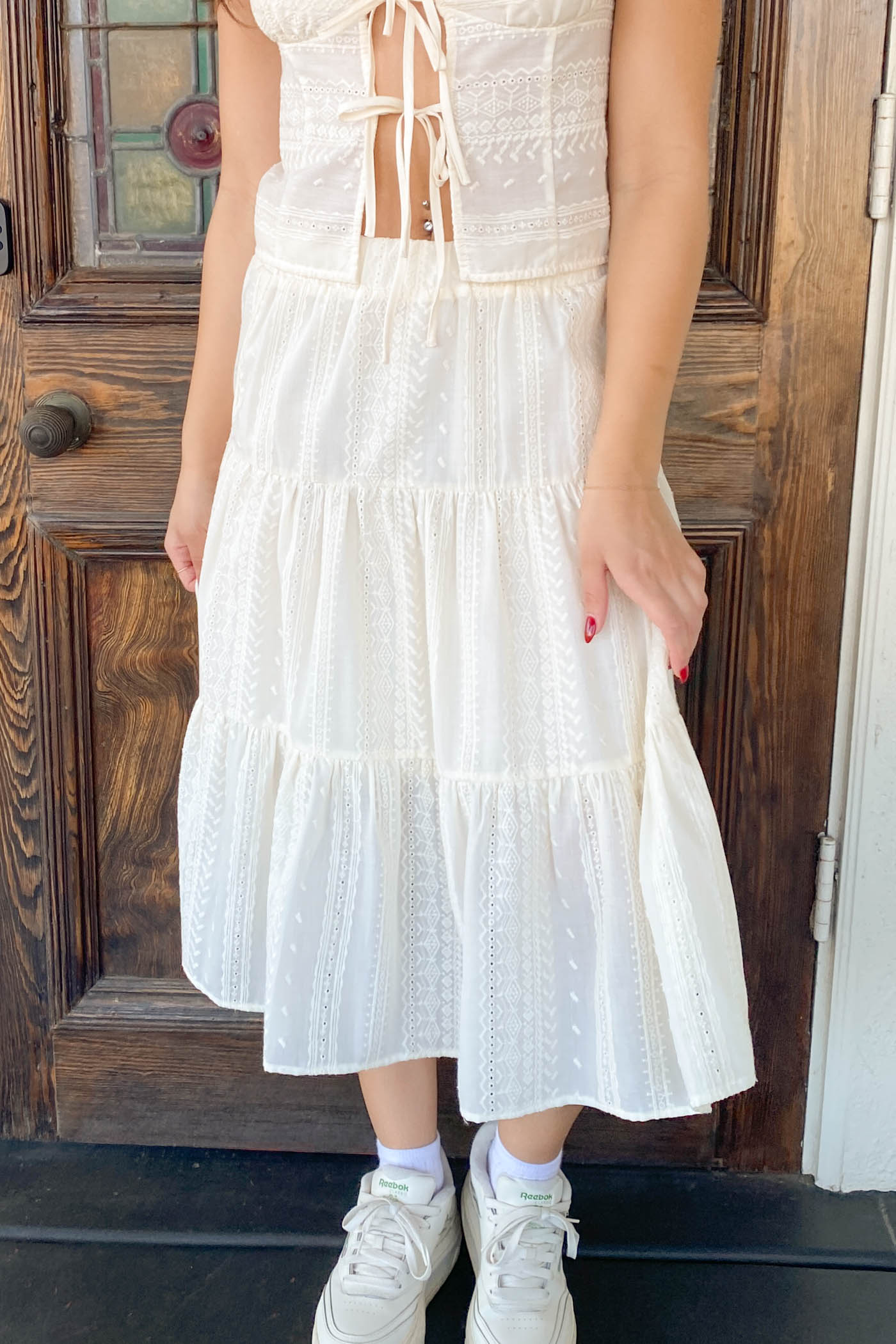 Person wearing a white dress standing in front of a wooden door.