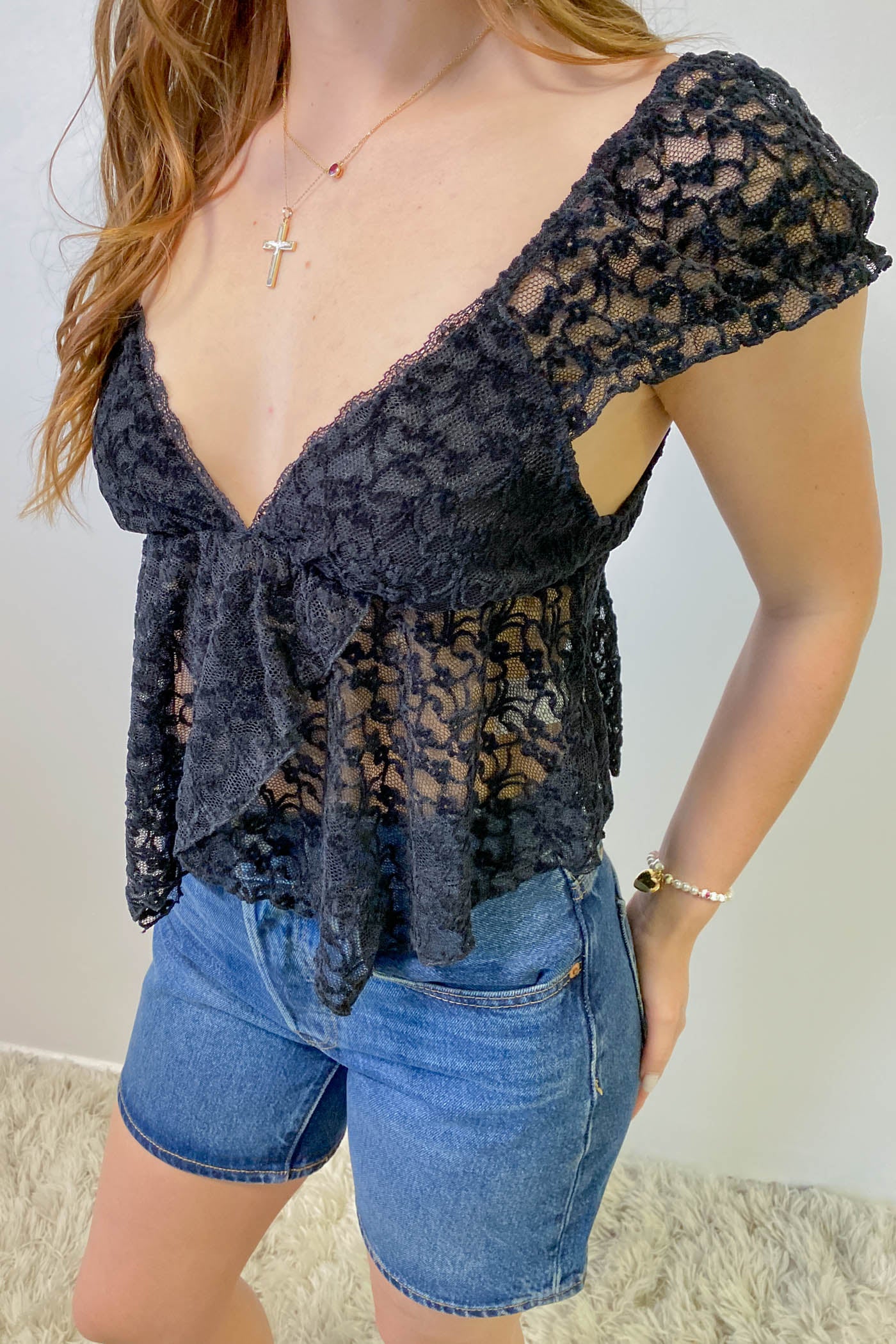 Person wearing a dark lace top and denim shorts against a neutral background
