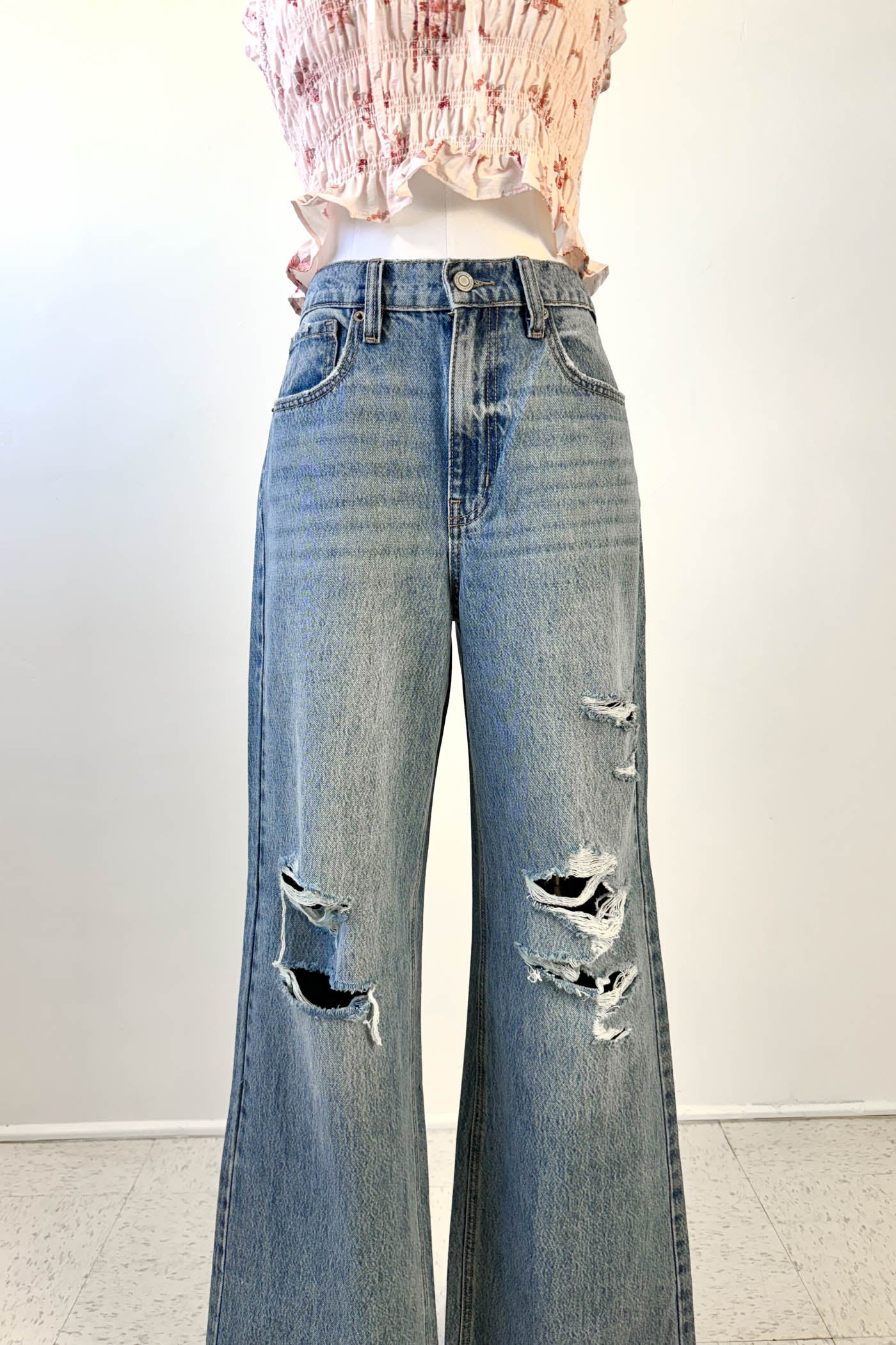 Distressed blue jeans worn by a person on a white background