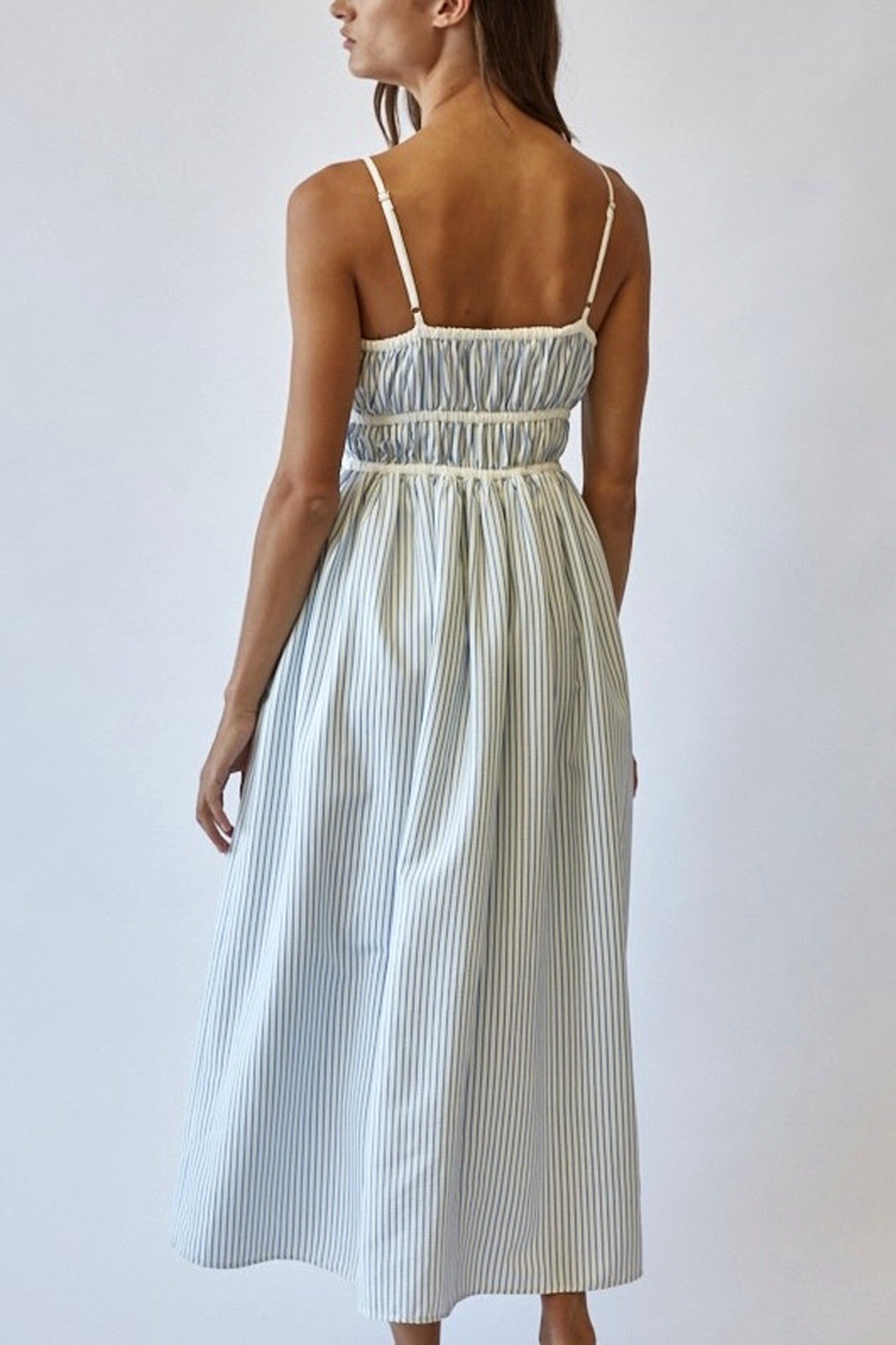 Woman wearing a white and blue striped dress against a plain background
