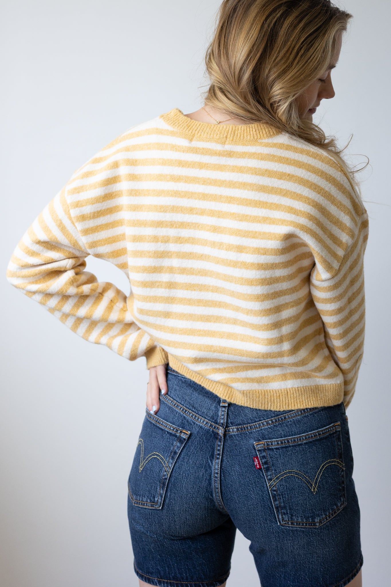 Person wearing a yellow and white striped sweater and blue jeans against a plain background