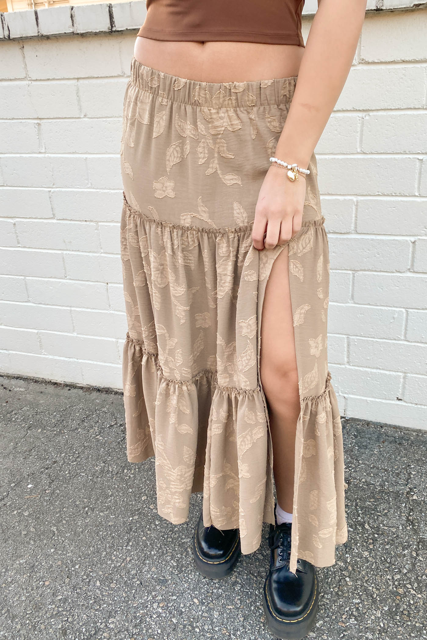 Person wearing a beige tiered skirt with a white brick wall background