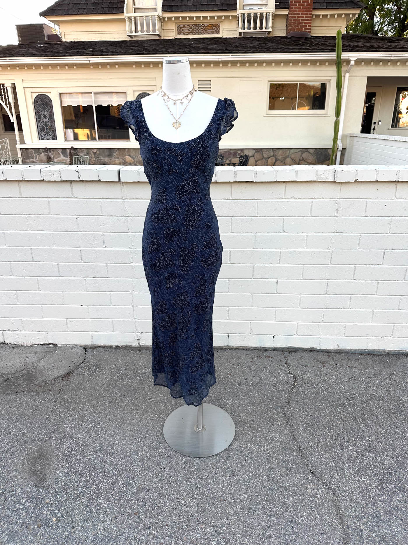 Navy blue dress on a mannequin in front of a white wall with a house in the background
