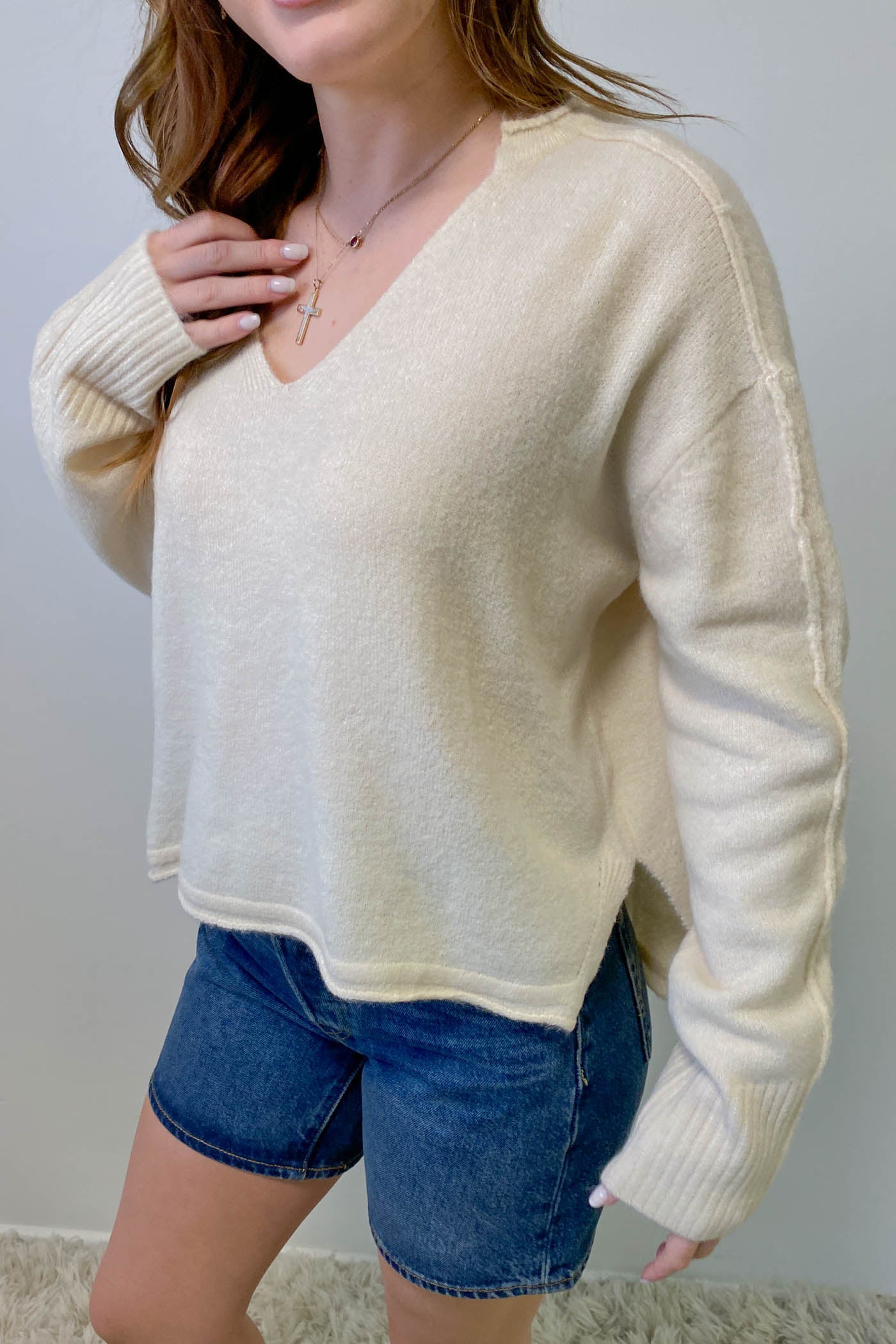 Person wearing a cream sweater and denim shorts against a plain background